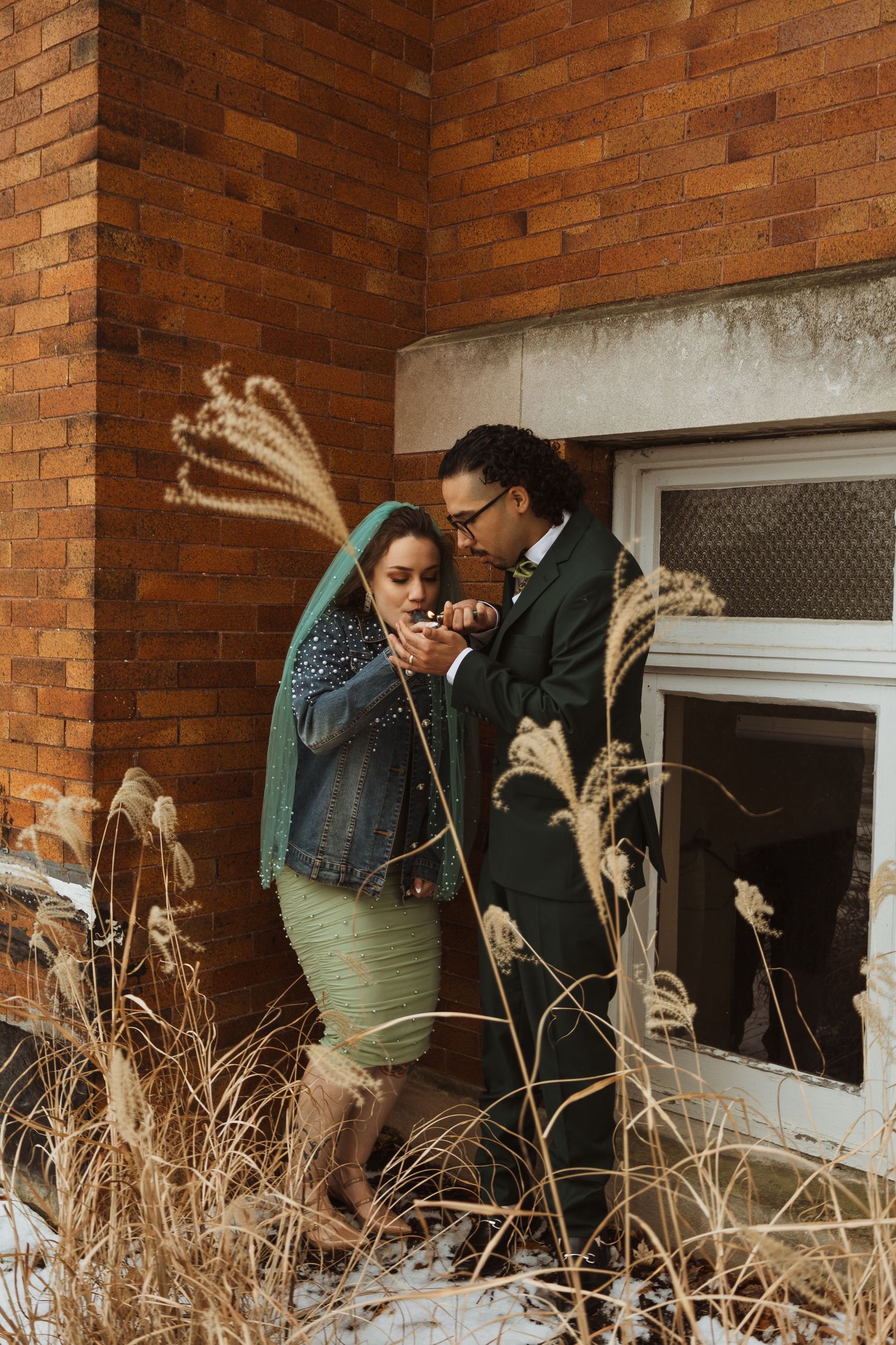 Bride and groom sharing a quiet moment outside a brick building in winter snow.
