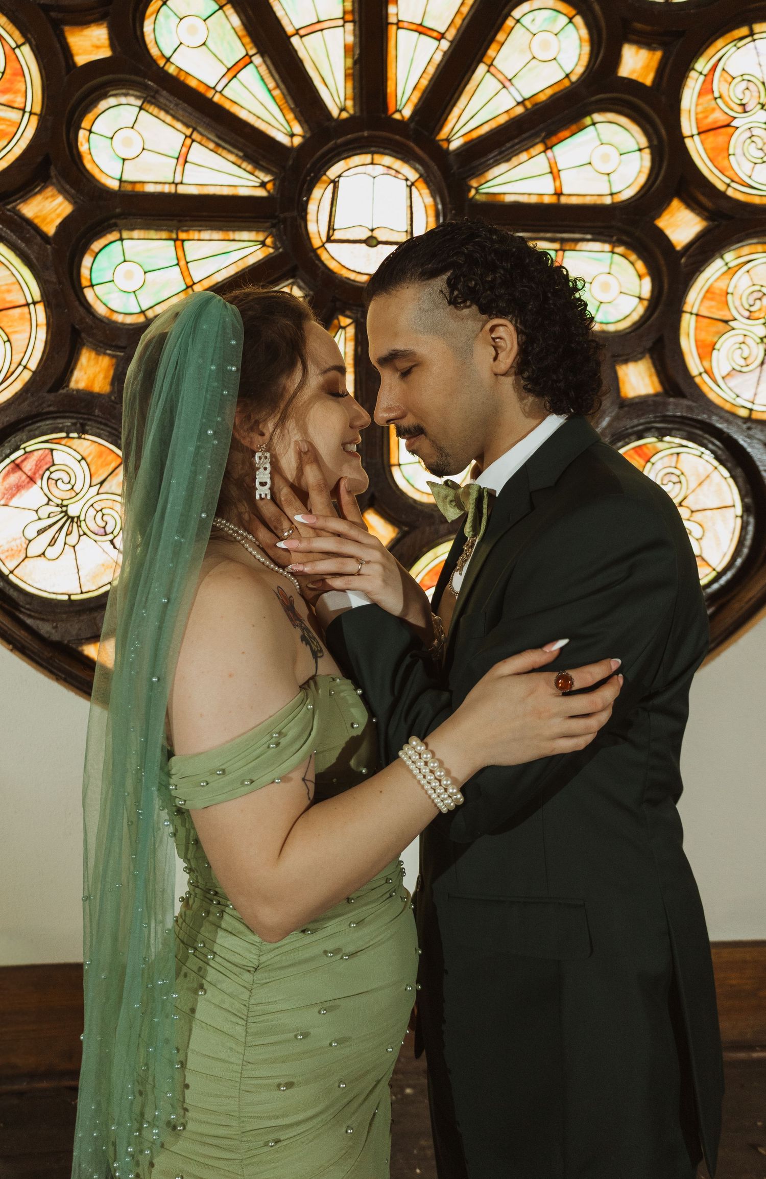 Bride and groom sharing romantic moment before stunning stained glass rose window in church.