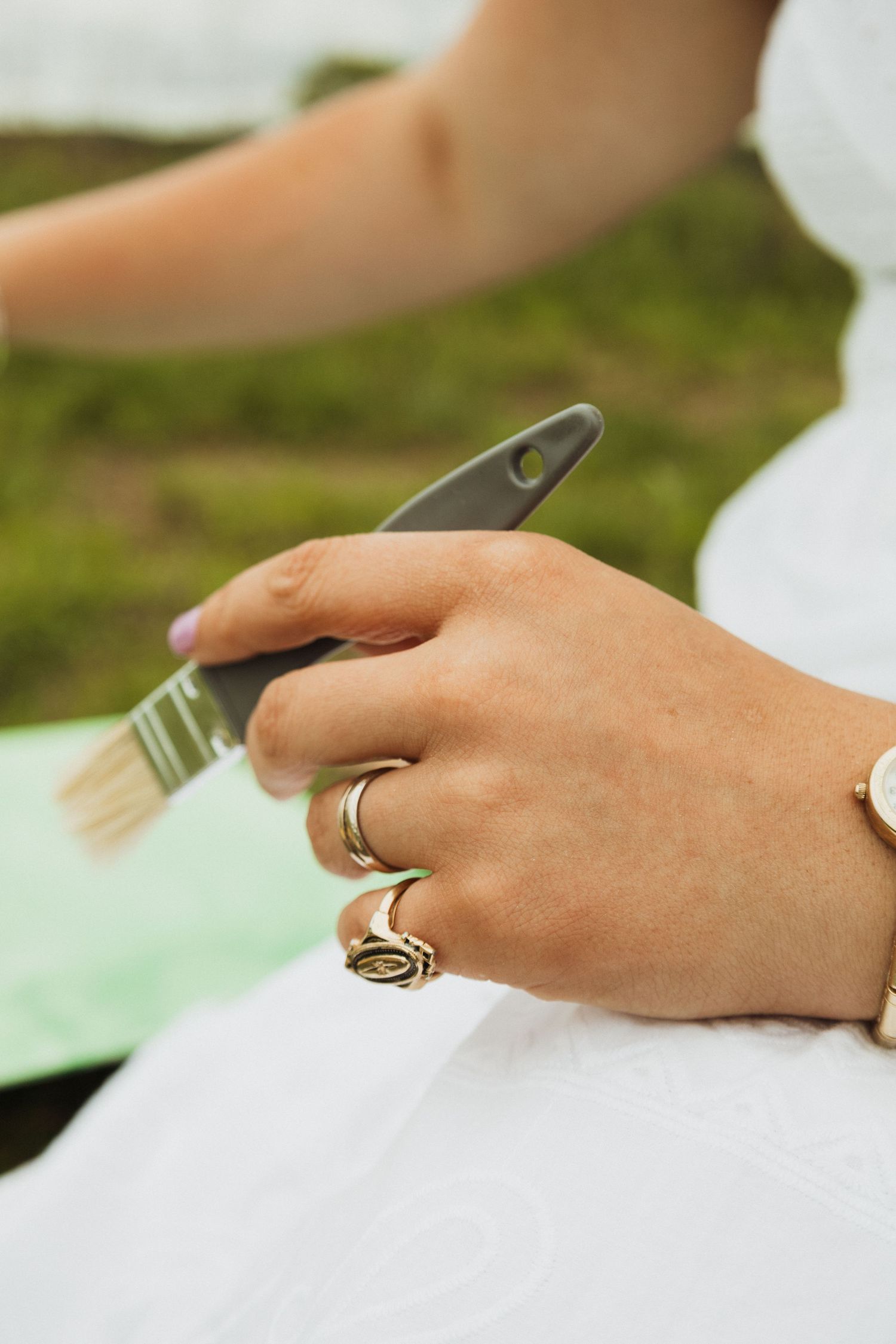 Hand with gold rings holding silverware over a white surface in an outdoor setting.