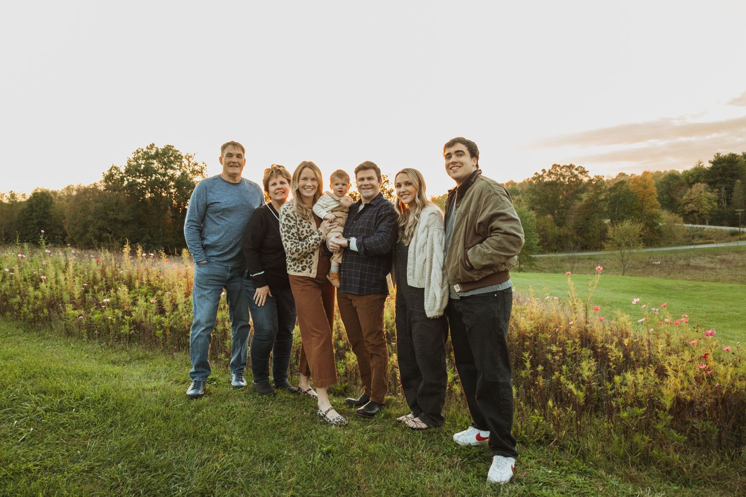 Group gathered outdoors against scenic autumn backdrop at sunset in grassy field.