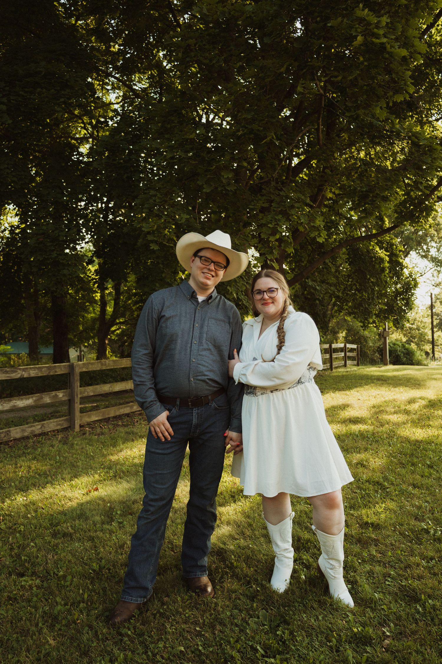 Country-western themed portrait session on grassy hillside with wooden fence backdrop.