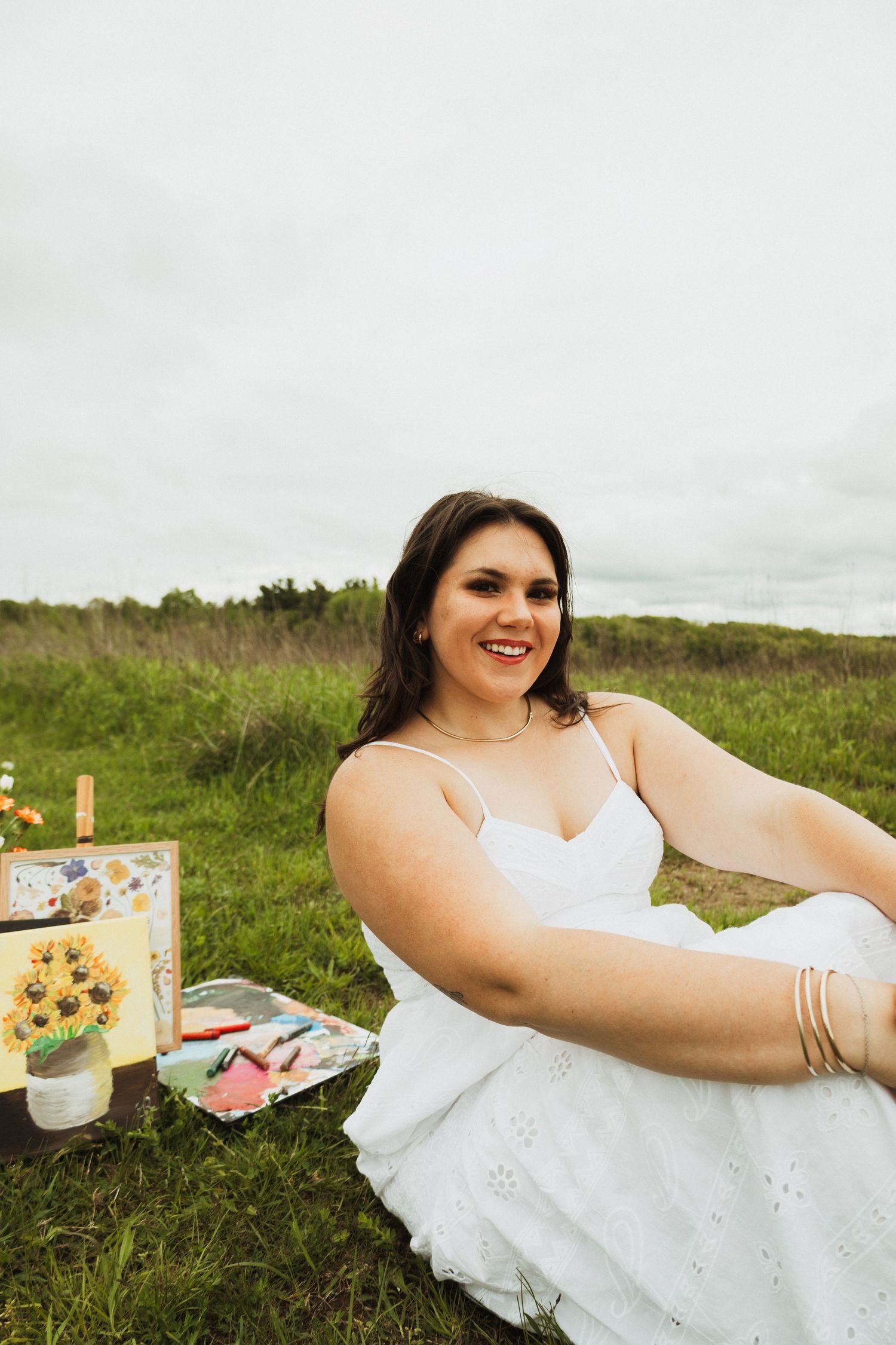 A romantic summer picnic scene in a grassy field with a white dress and decorative boxes laid out on the ground.