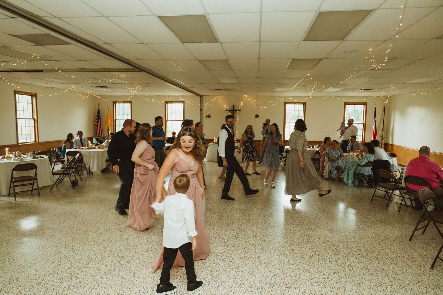 Panoramic shot of a church hall decorated with string lights showing people dancing and celebrating.