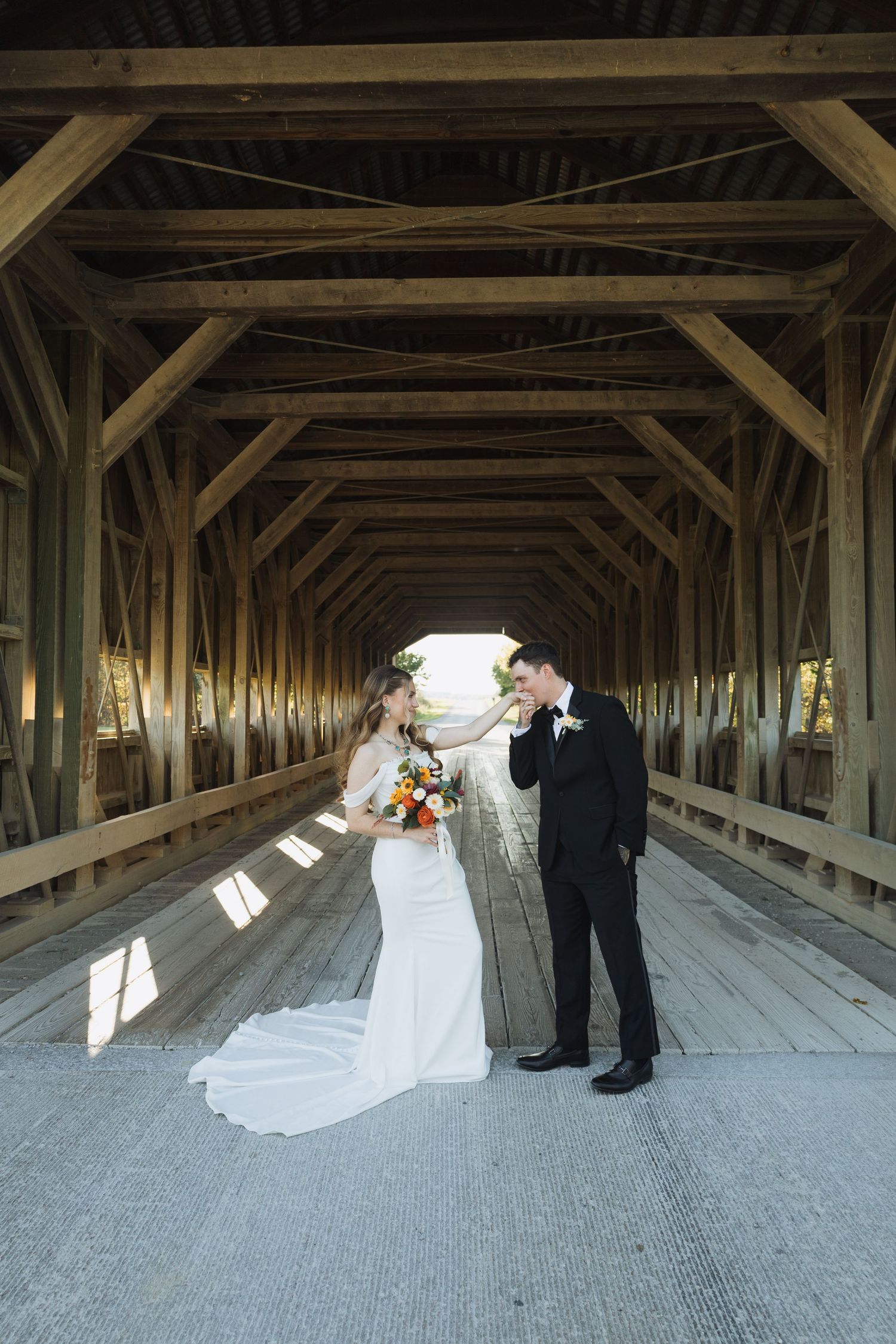 Wedding couple posing in a rustic covered wooden bridge with dramatic lighting and architecture.