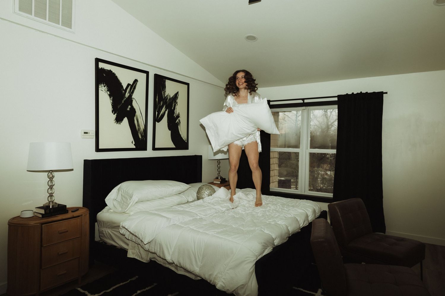 Person in white robe poses energetically on bed with decorative bird prints on wall.