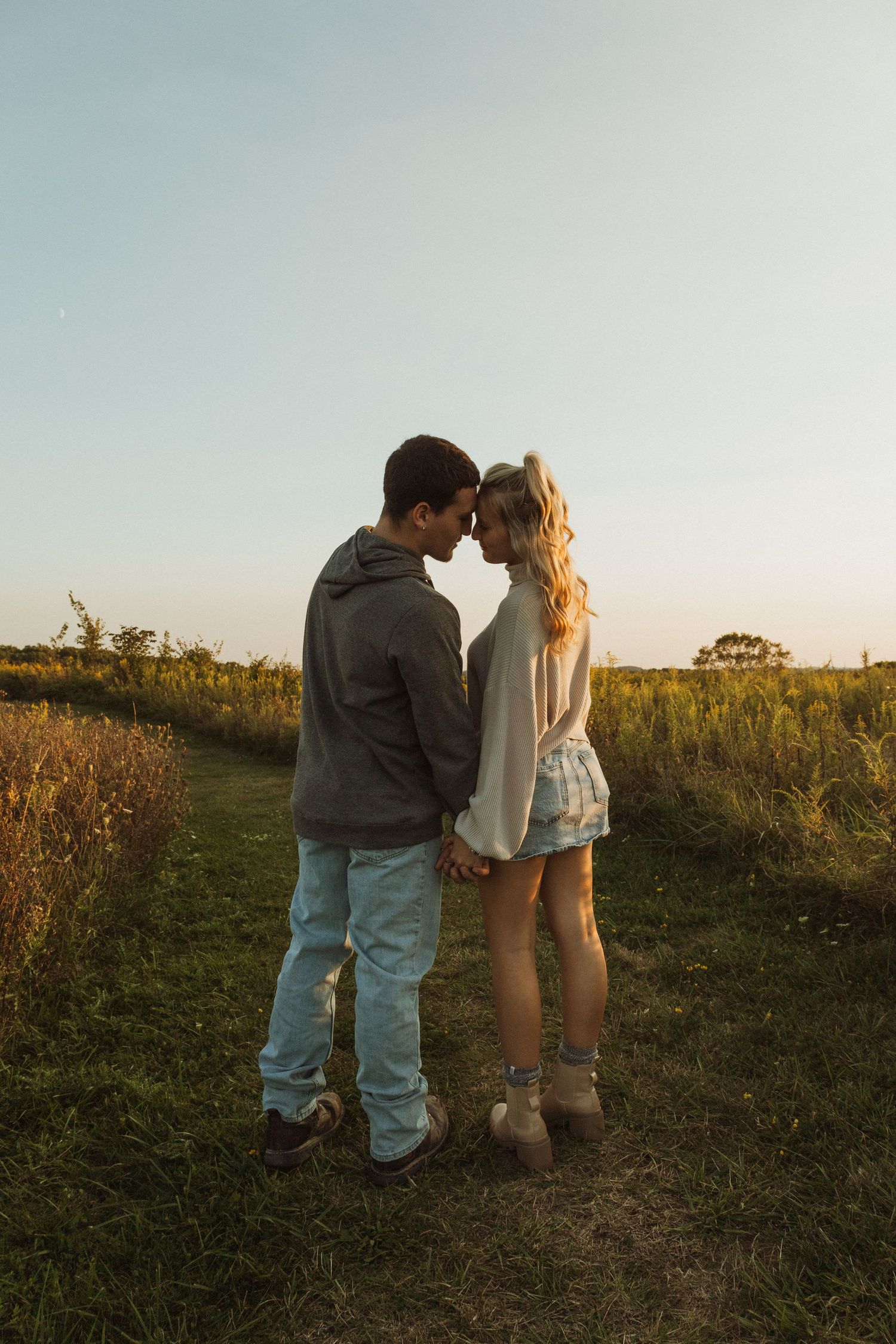 Intimate moment between couple standing in grassy field at sunset.