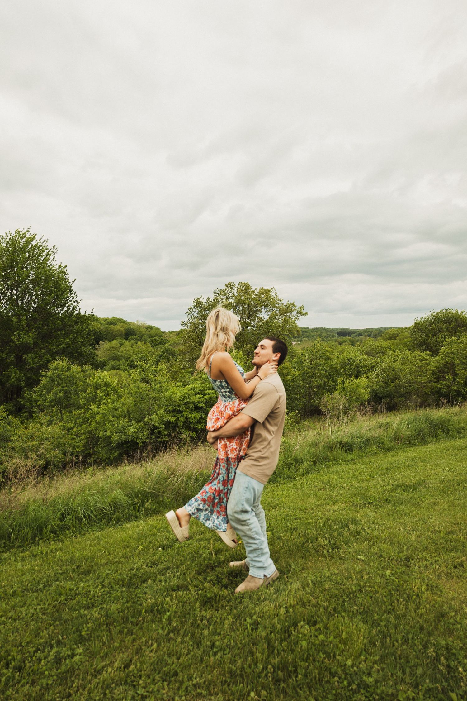 A joyful couple shares a playful dance move on a lush green hillside landscape.