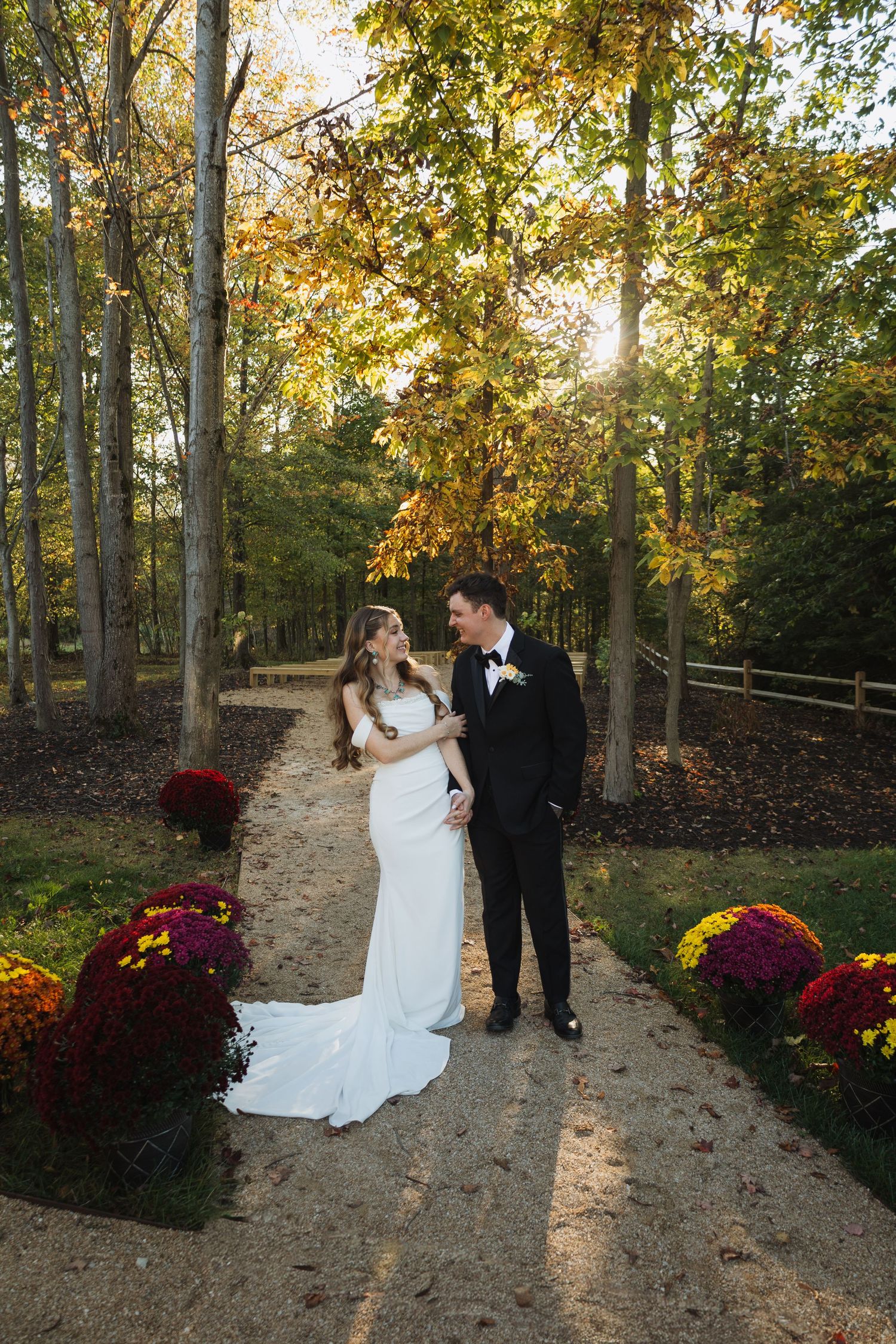 A romantic wedding portrait on a tree-lined path decorated with burgundy mums in autumn.