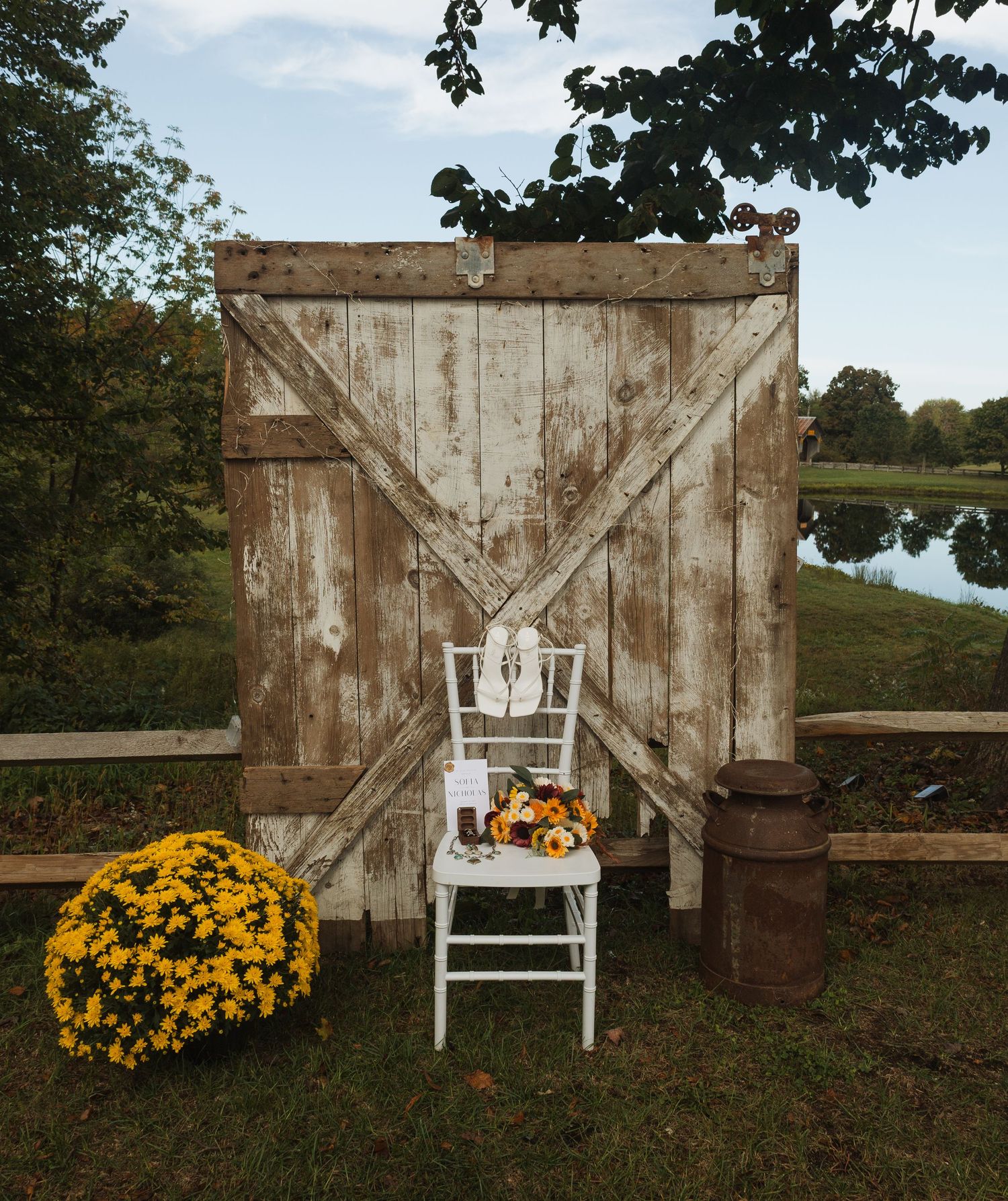 Rustic barn door backdrop with white chair and yellow mums creating a charming outdoor wedding setting.