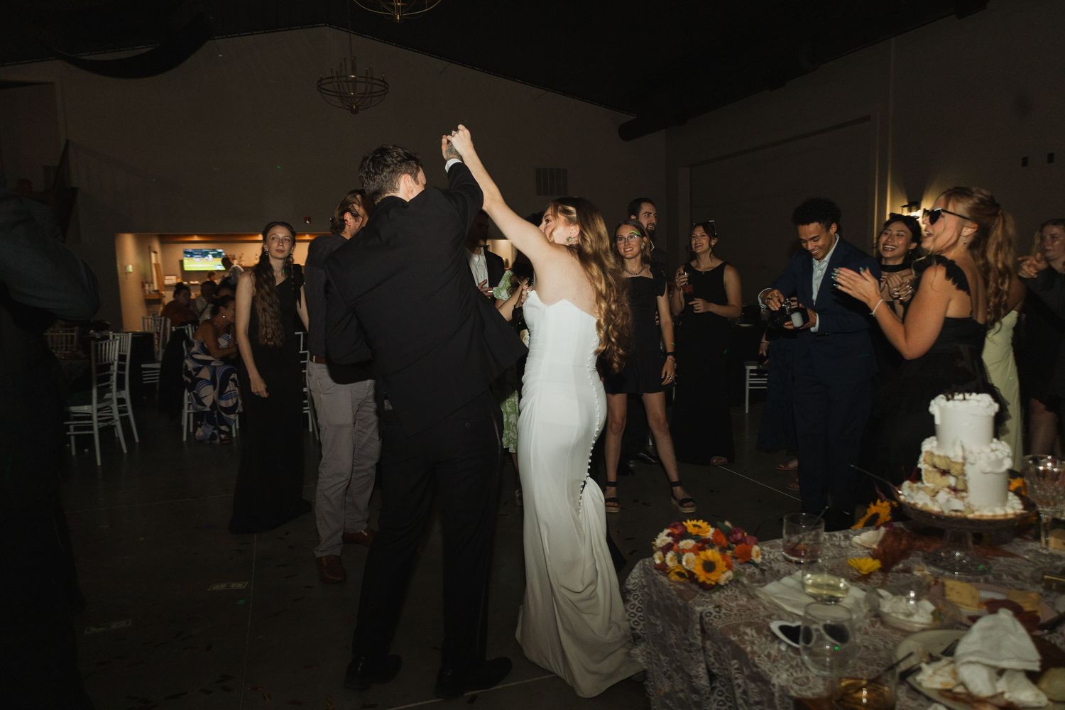 Wedding reception celebration with guests dancing in a dark venue with decorative lighting.