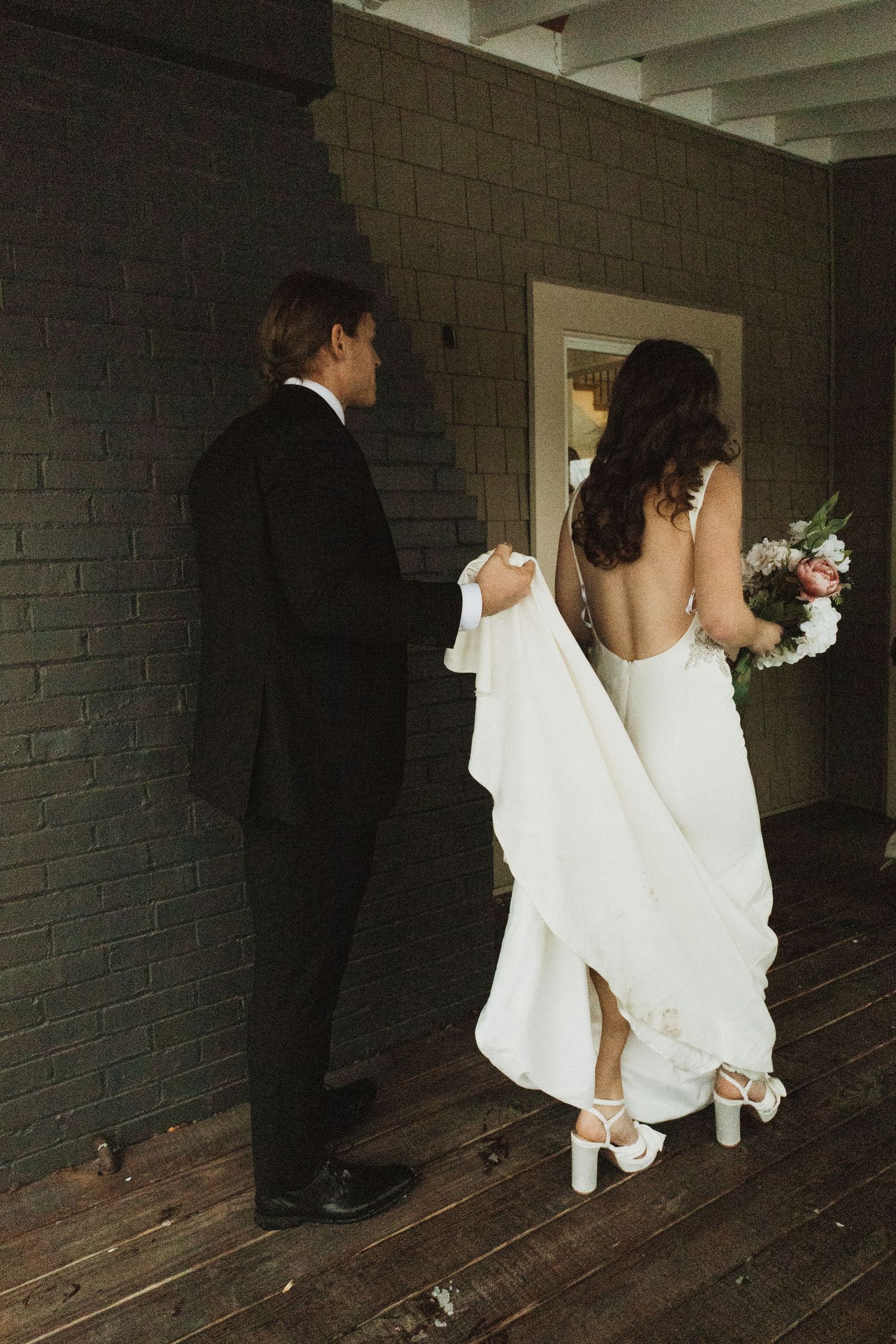 A couple in formal attire walking on a dark wooden deck outside.
