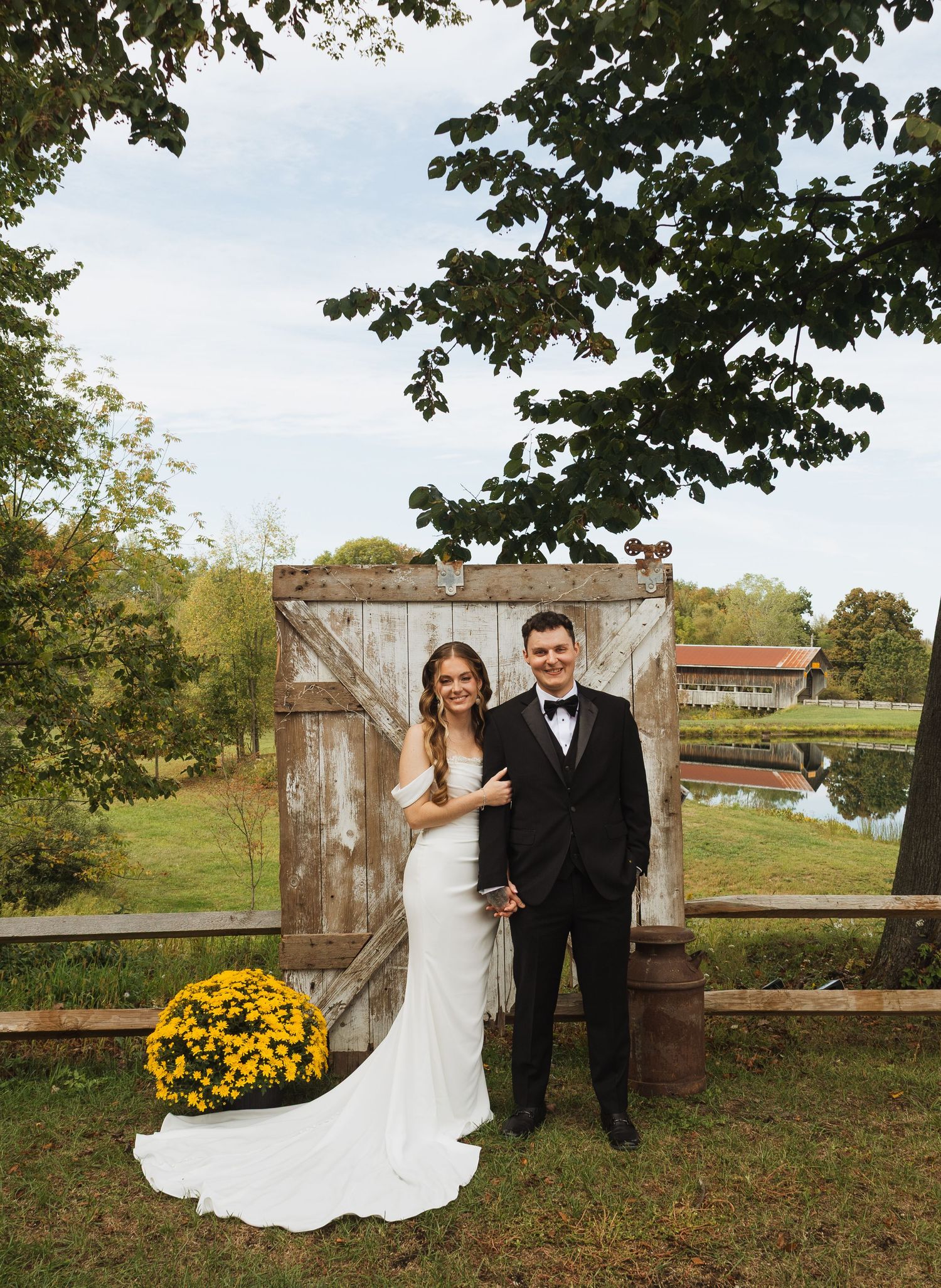 Rustic outdoor wedding venue with wooden gates and yellow mums in autumn setting.