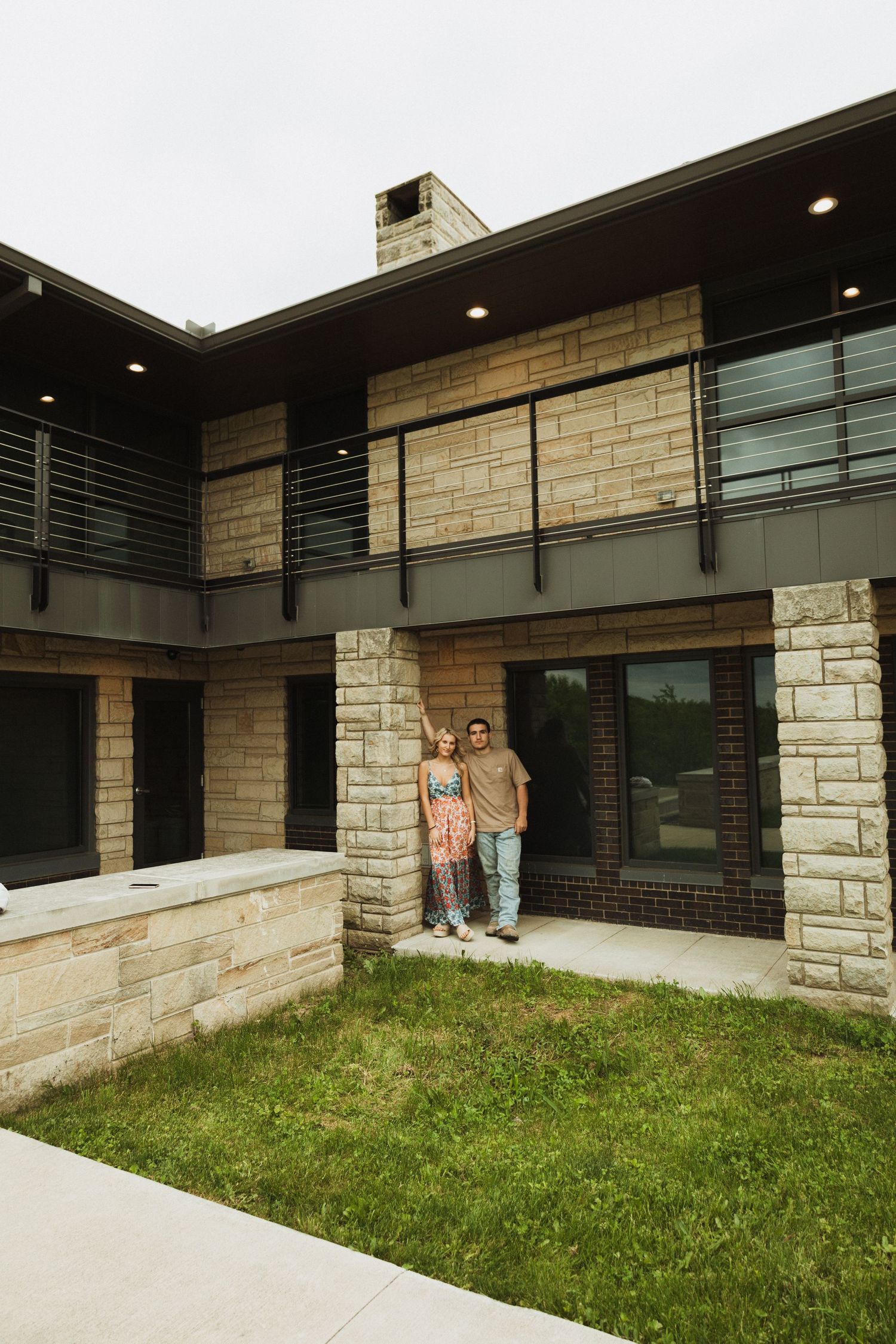 A modern stone and glass house exterior with a couple standing in the entrance on a summer day.