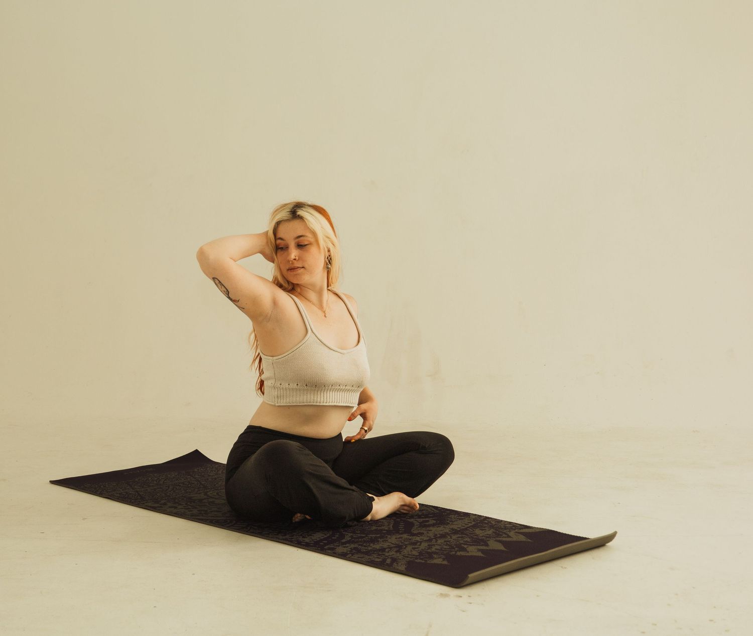 Minimalist studio portrait featuring person in light-colored top relaxing on dark mat.