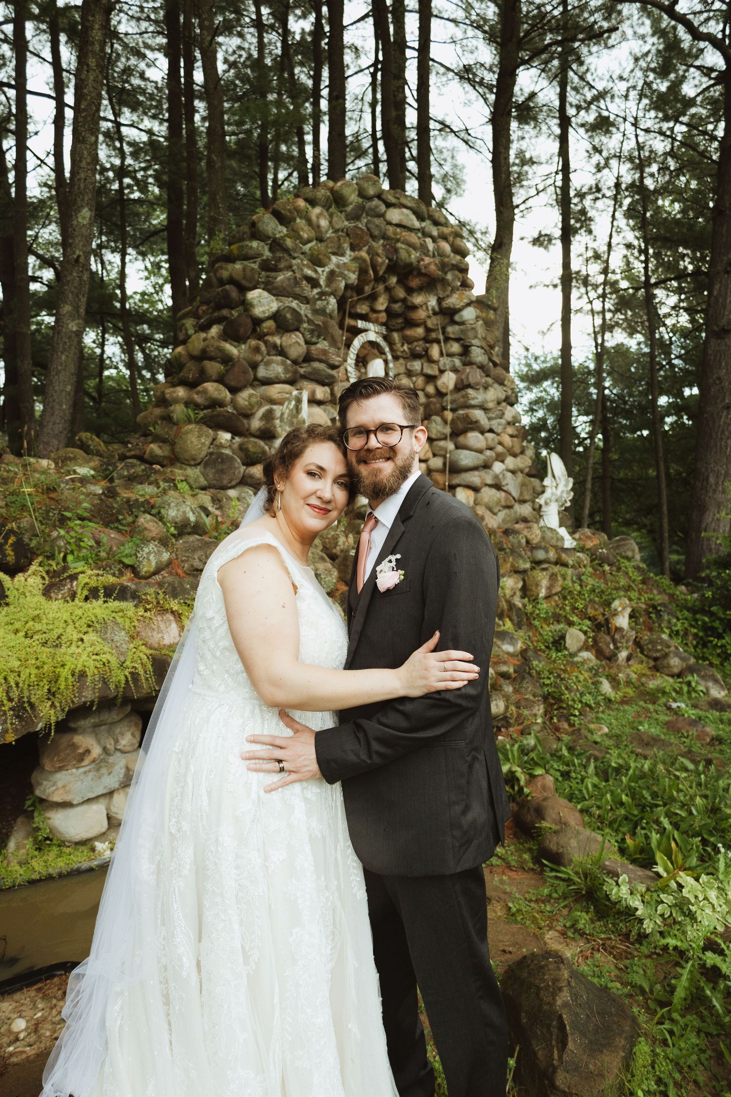 A couple shares an intimate moment in a wooded area with stone walls during their wedding photoshoot.