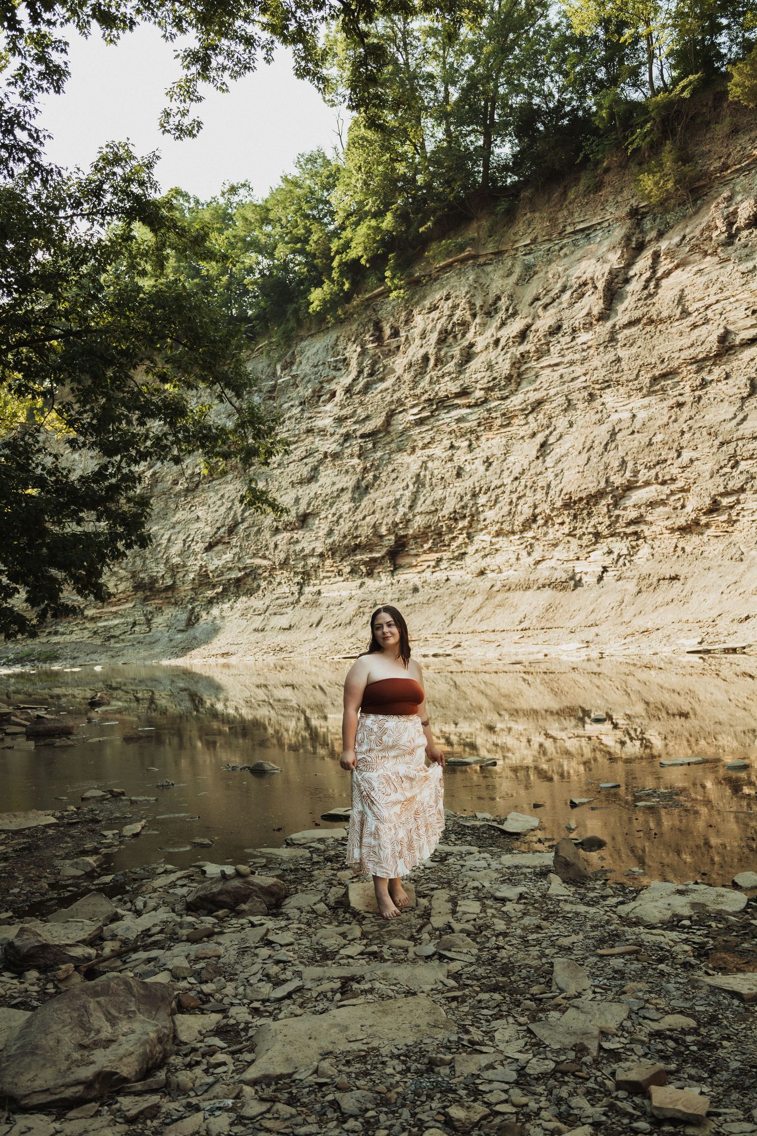 A scenic view of a rocky creek bed with limestone cliffs and dense forest in the background.