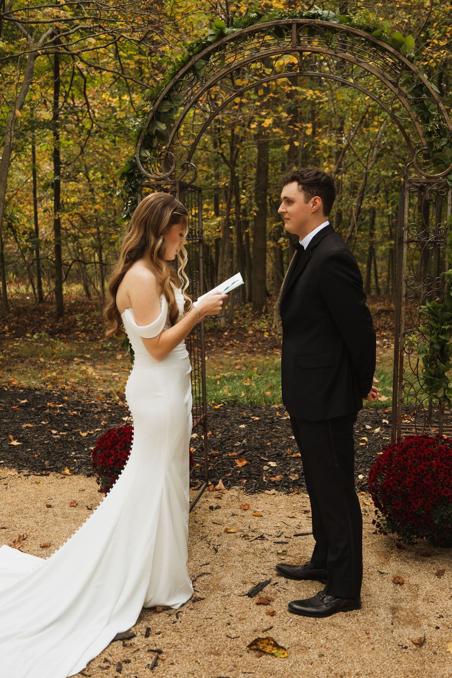 First look wedding moment captured in autumn forest with bride in white dress and burgundy flowers.