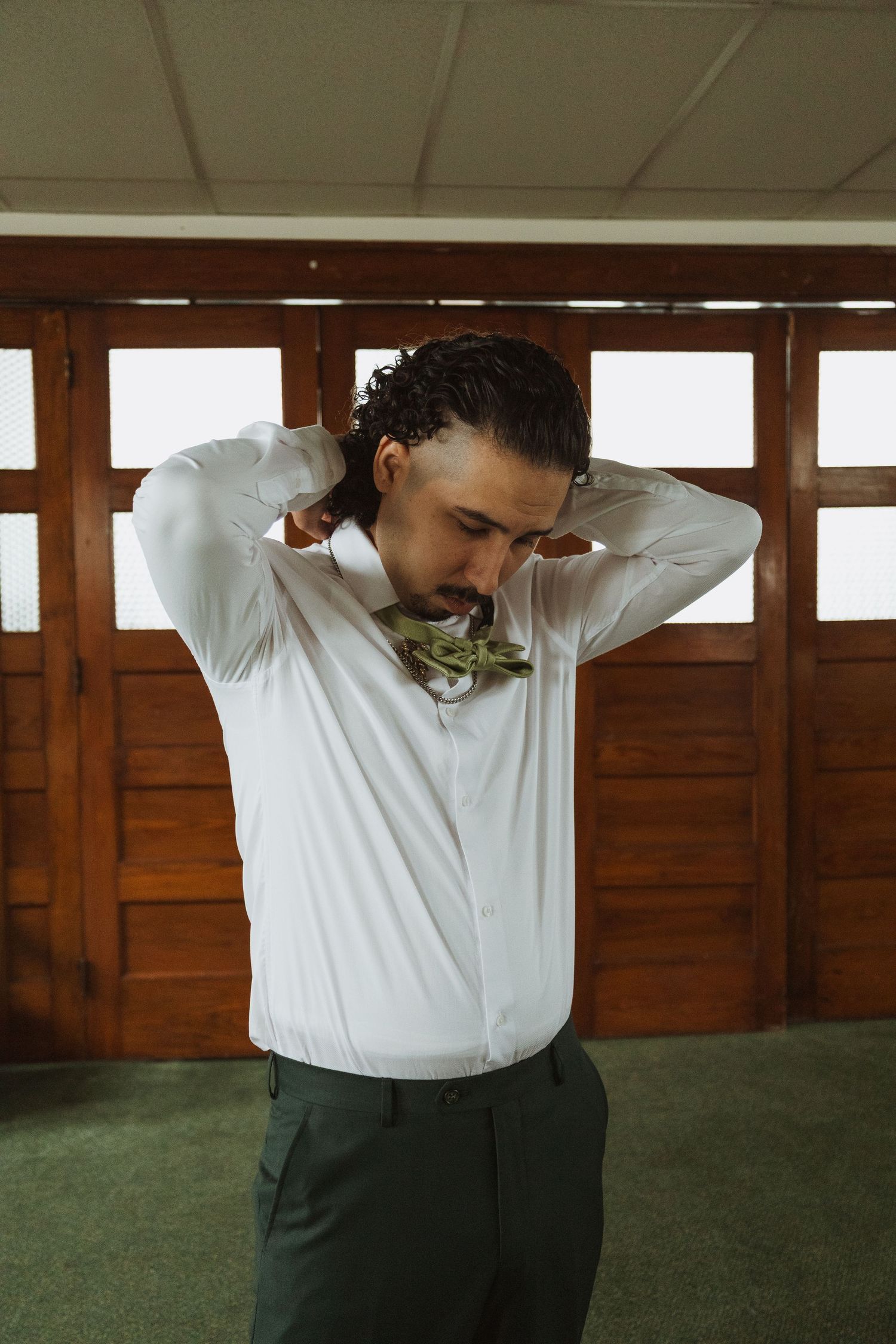 Groom in white shirt adjusting green floral bow tie before wedding ceremony.
