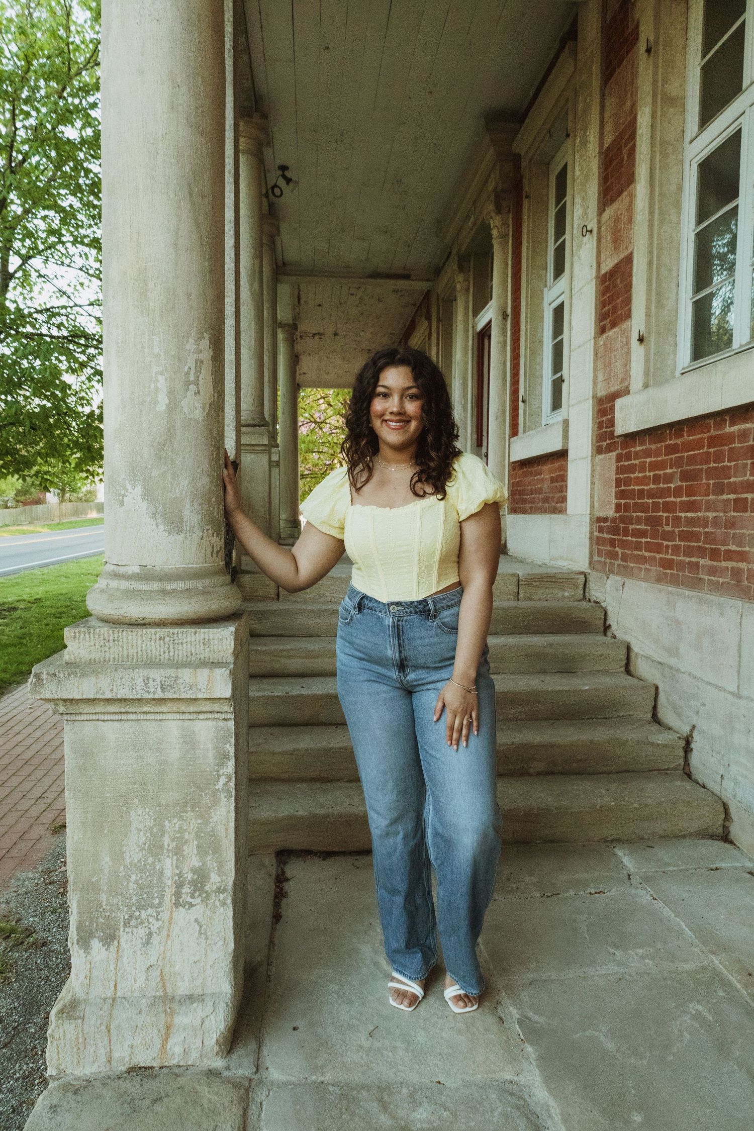 Casual portrait on historic building steps featuring jeans and a white top with classical columns.