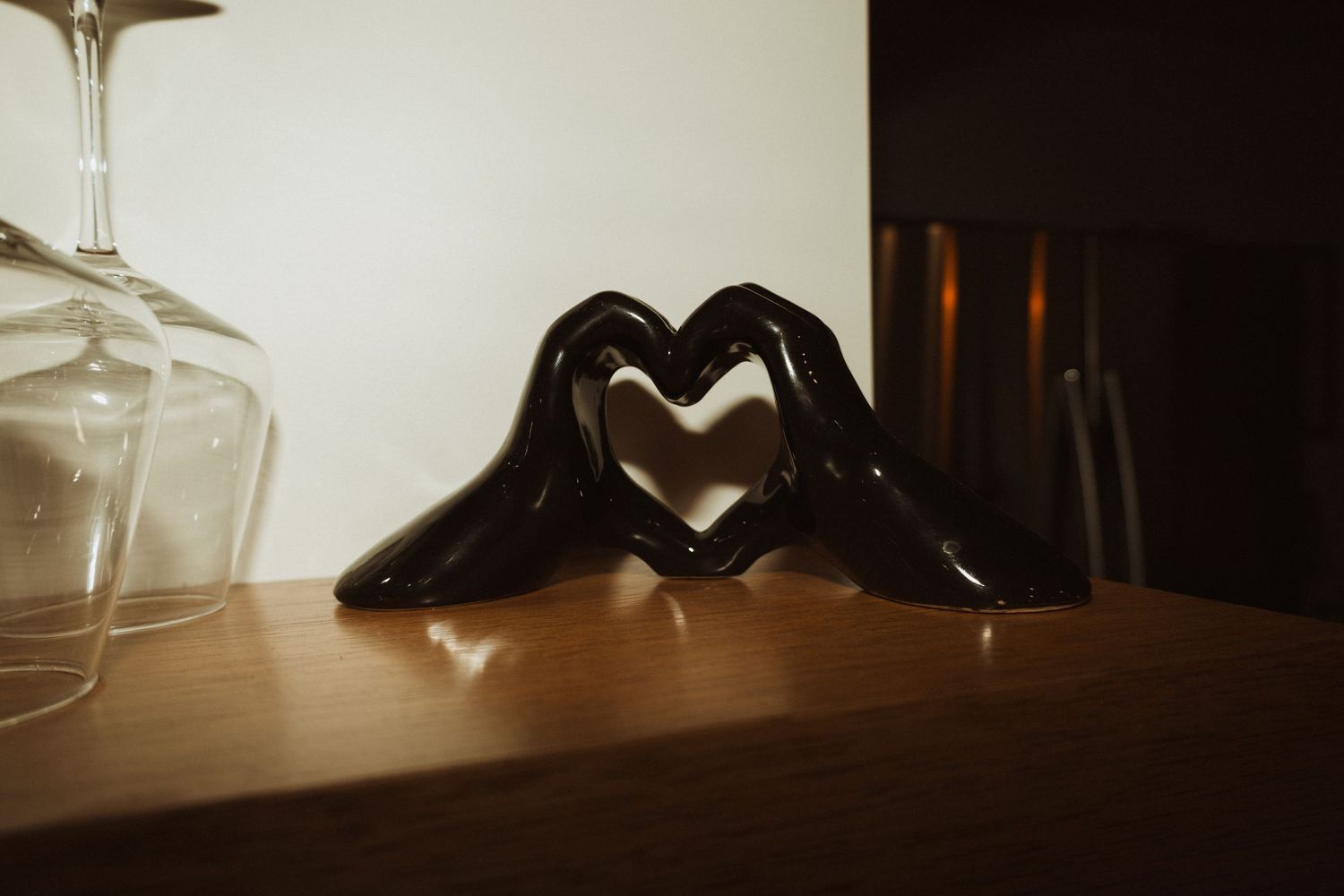 Hands forming a heart shadow on a wooden surface in moody lighting.