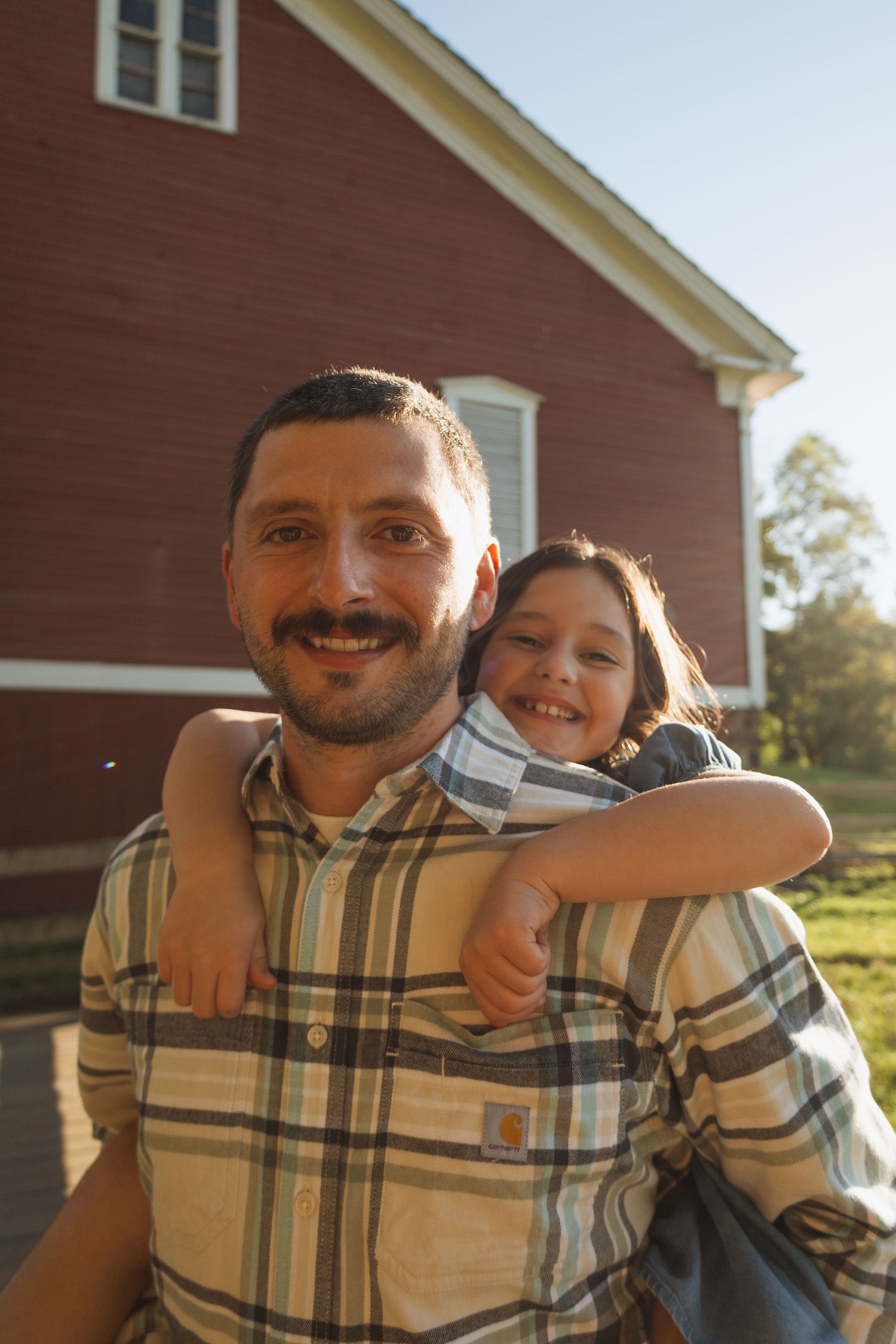 A heartwarming series of candid moments between a parent and child laughing together against a red barn background.