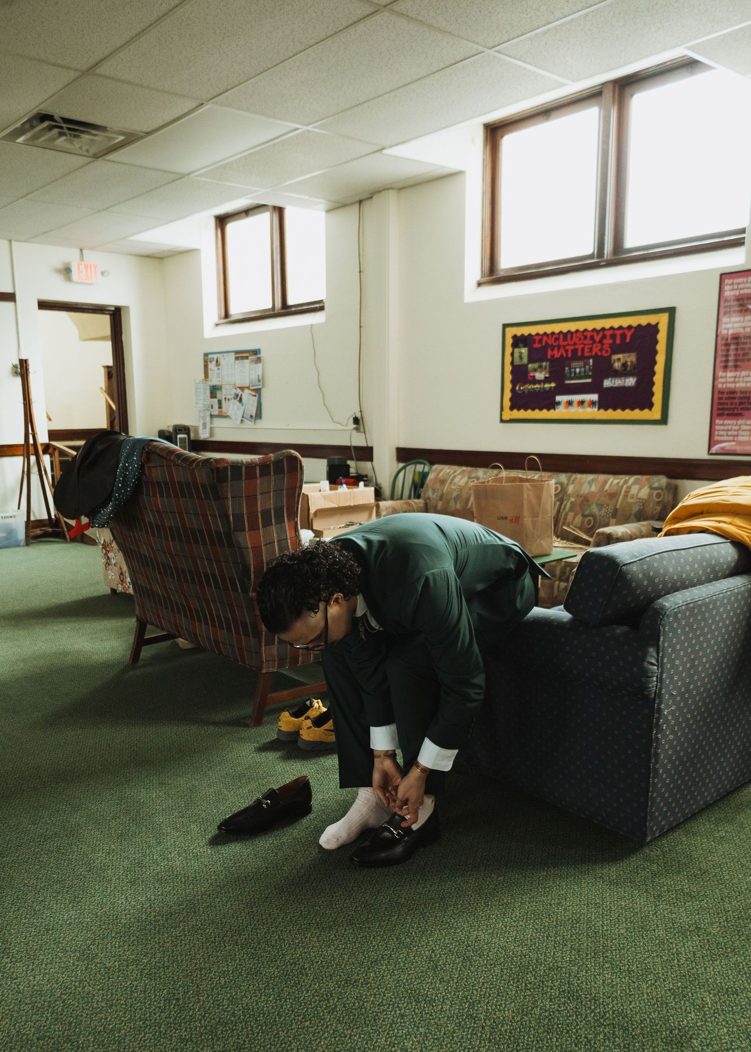 Groom in dark green suit putting on shoes in casual lounge room before wedding.