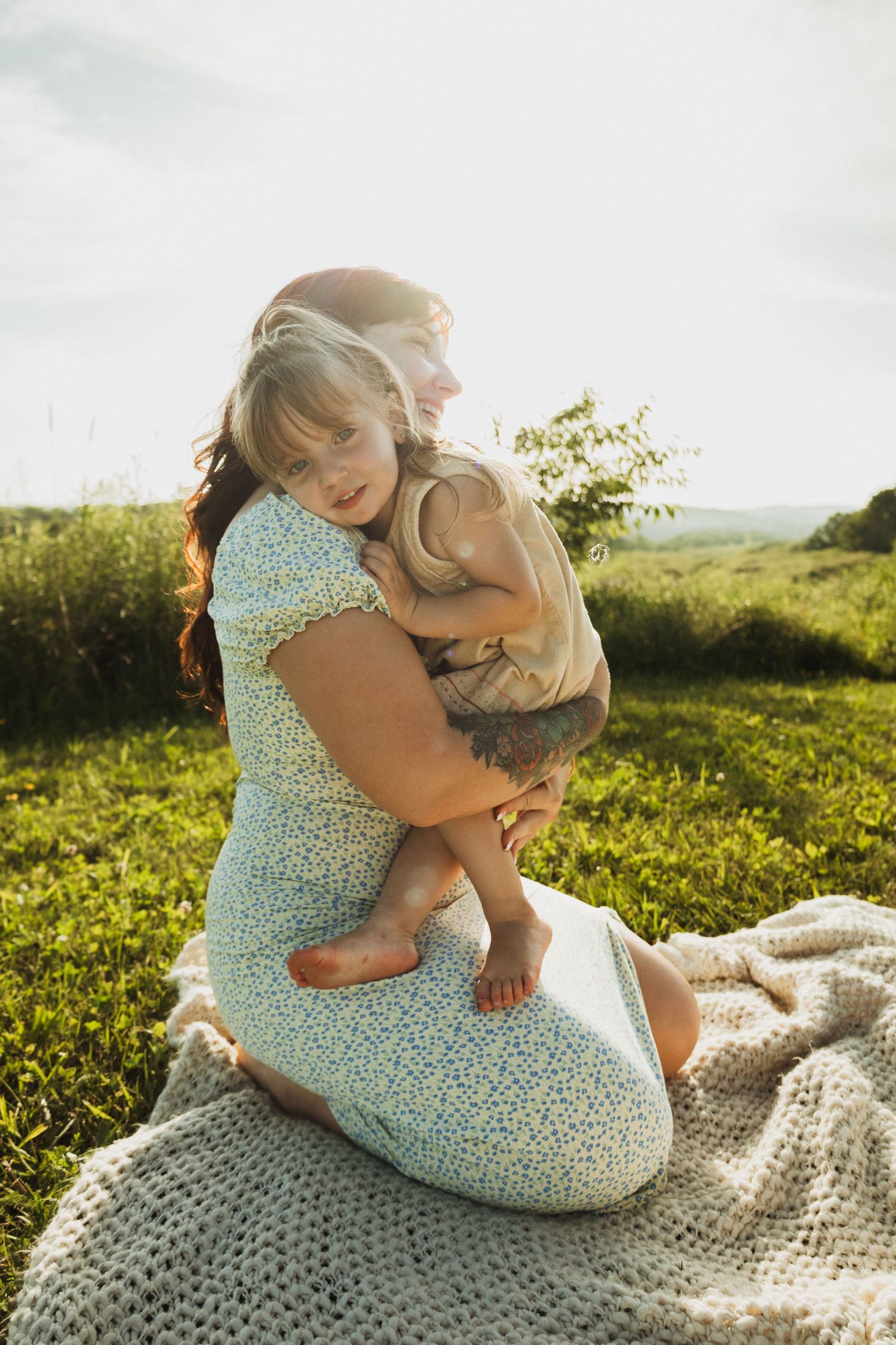 Tender family moment on a crocheted blanket in a sunlit grassy field.