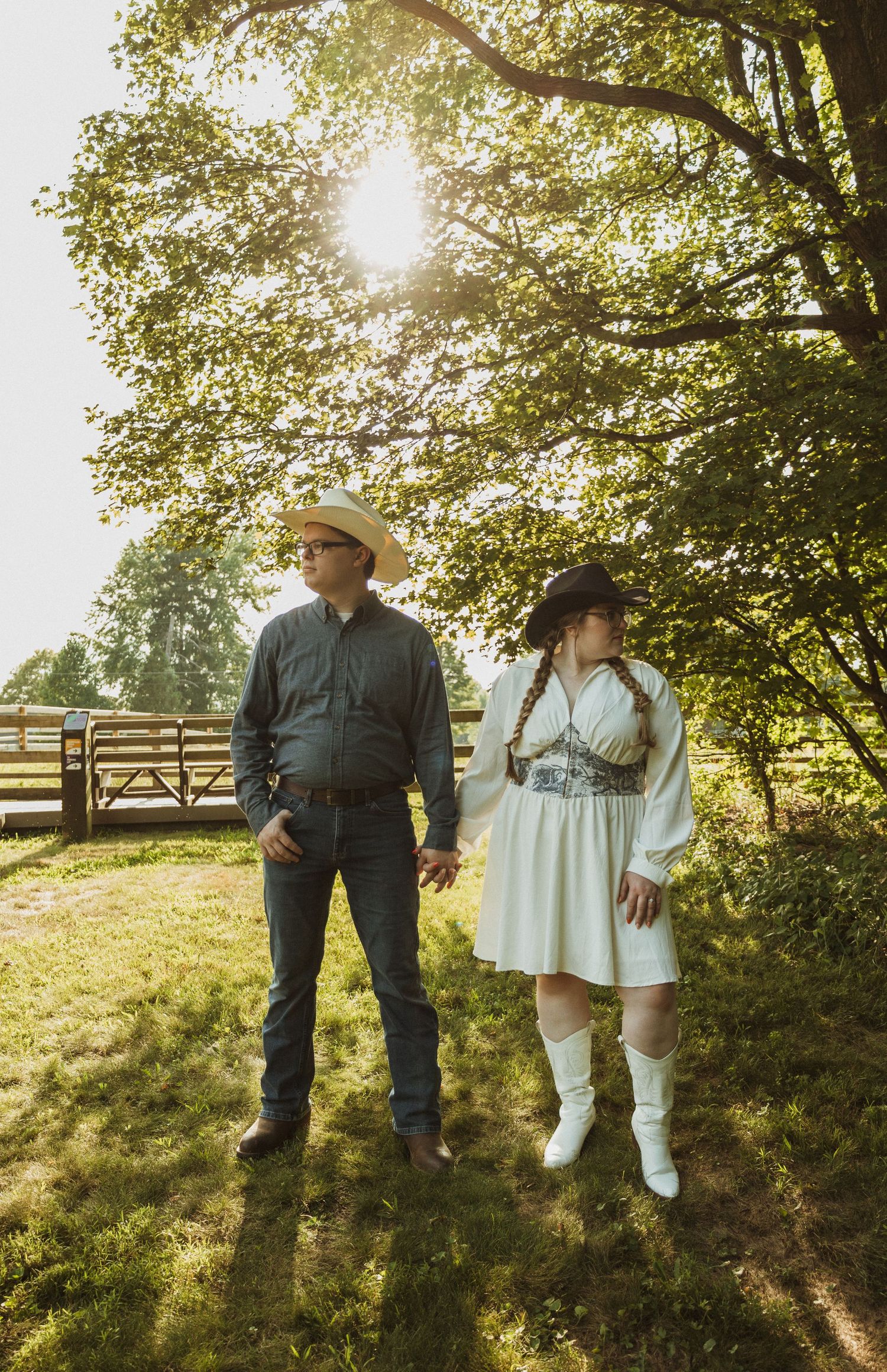 Couple in western attire walking through sunlit meadow.