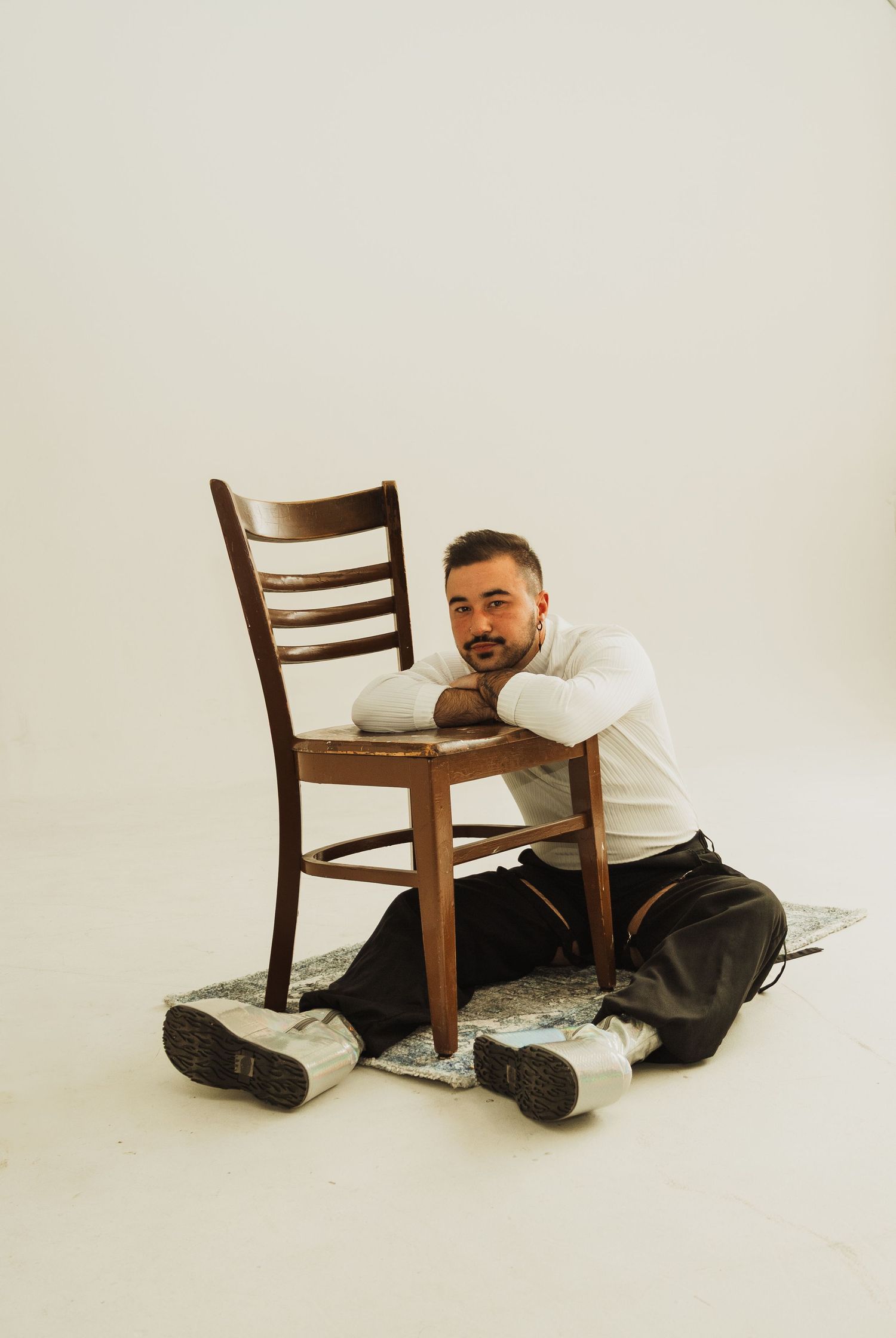 Artistic portrait in minimalist studio with person lounging on wooden chair against white background.