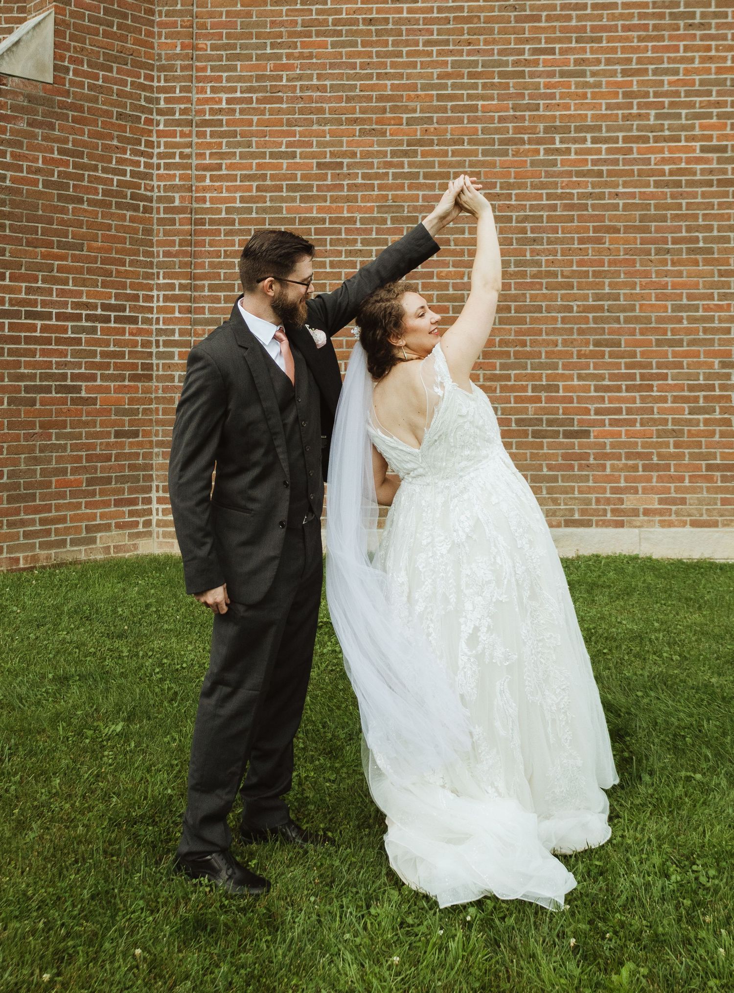 Couple shares romantic dance pose against brick wall backdrop outdoors.