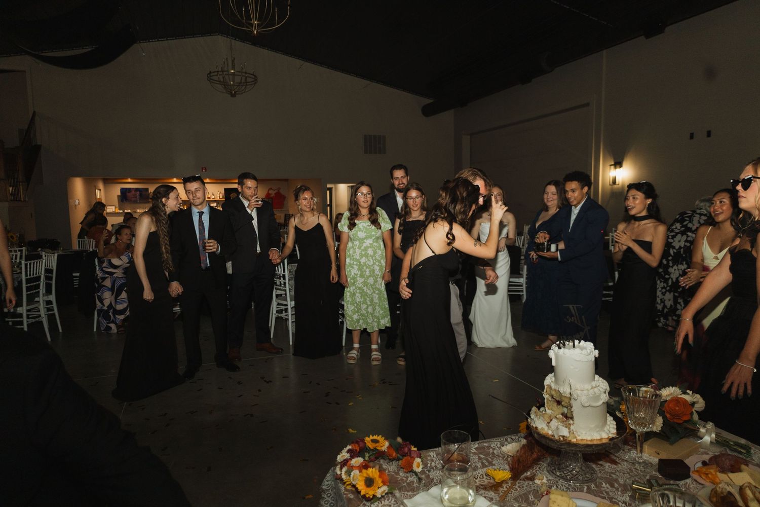 Wedding guests gather in a dark reception hall with elegant table settings and decorations.