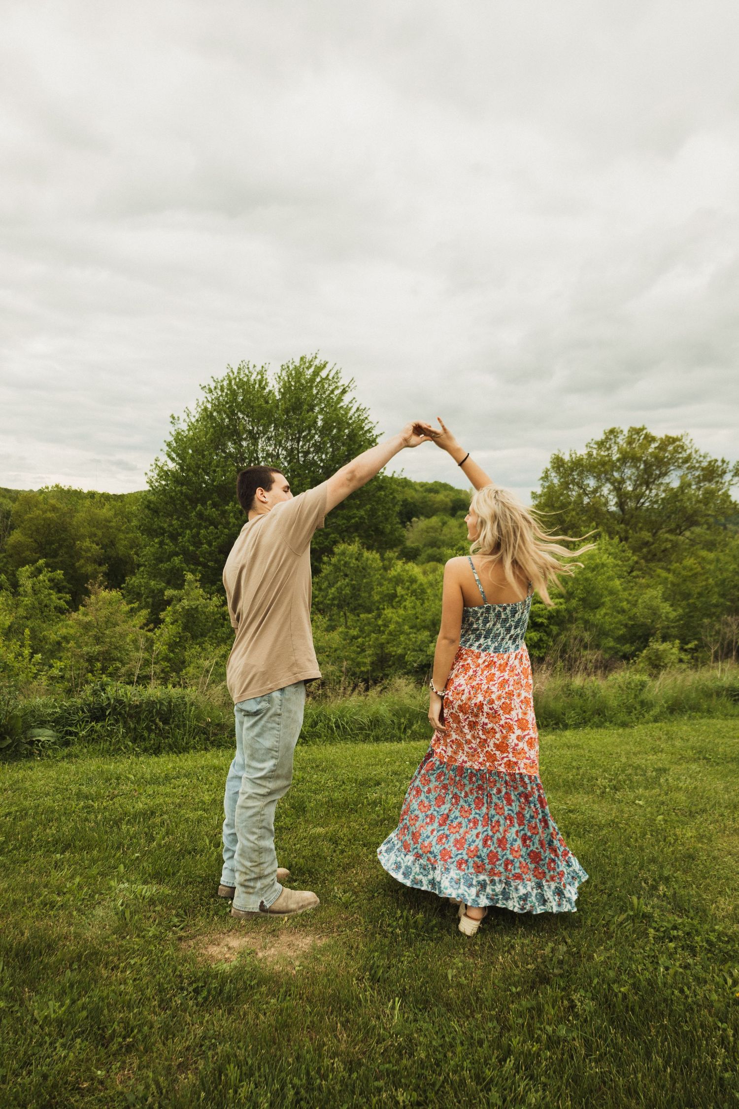 A couple performs a twirling dance move on a grassy hilltop during an overcast day.