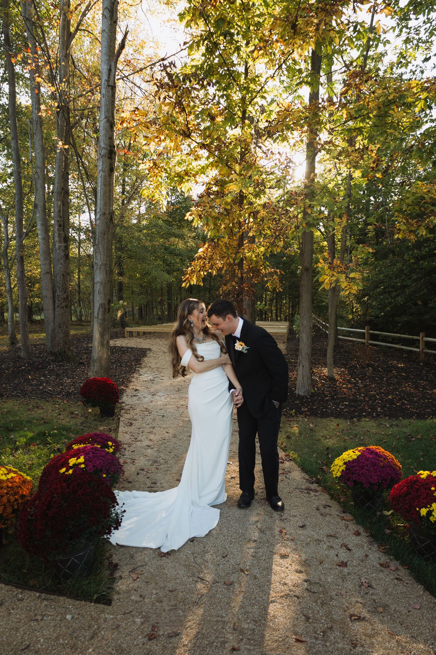 Couple sharing romantic moments on a fall path decorated with vibrant mums and autumn foliage.