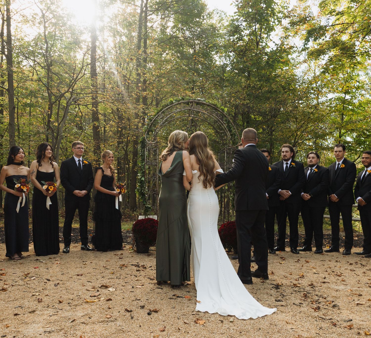 Outdoor forest wedding ceremony with guests standing in rows among autumn trees.