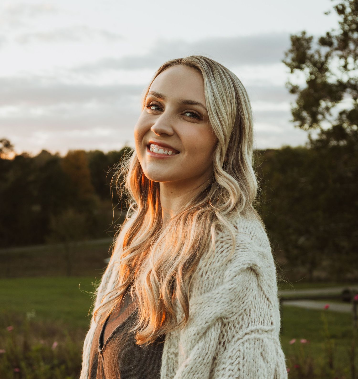 Portrait of person in white sweater during golden hour with natural landscape backdrop.