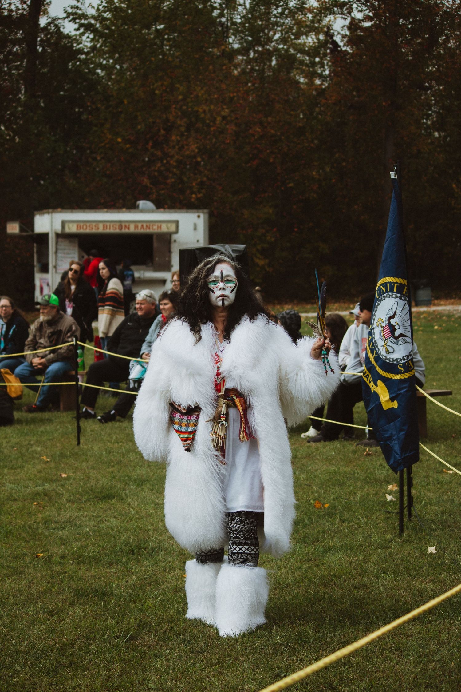A performer in white furry costume and face paint participates in a cultural celebration.