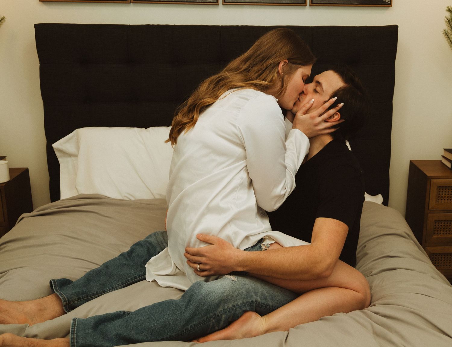 Intimate moment on grey bedding with black headboard and modern wall decor.