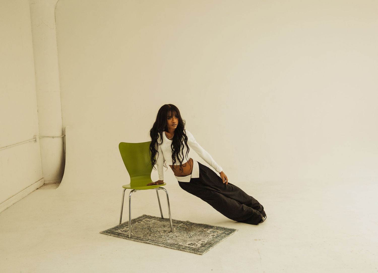 Studio portrait with person reclining beside green chair on decorative rug.