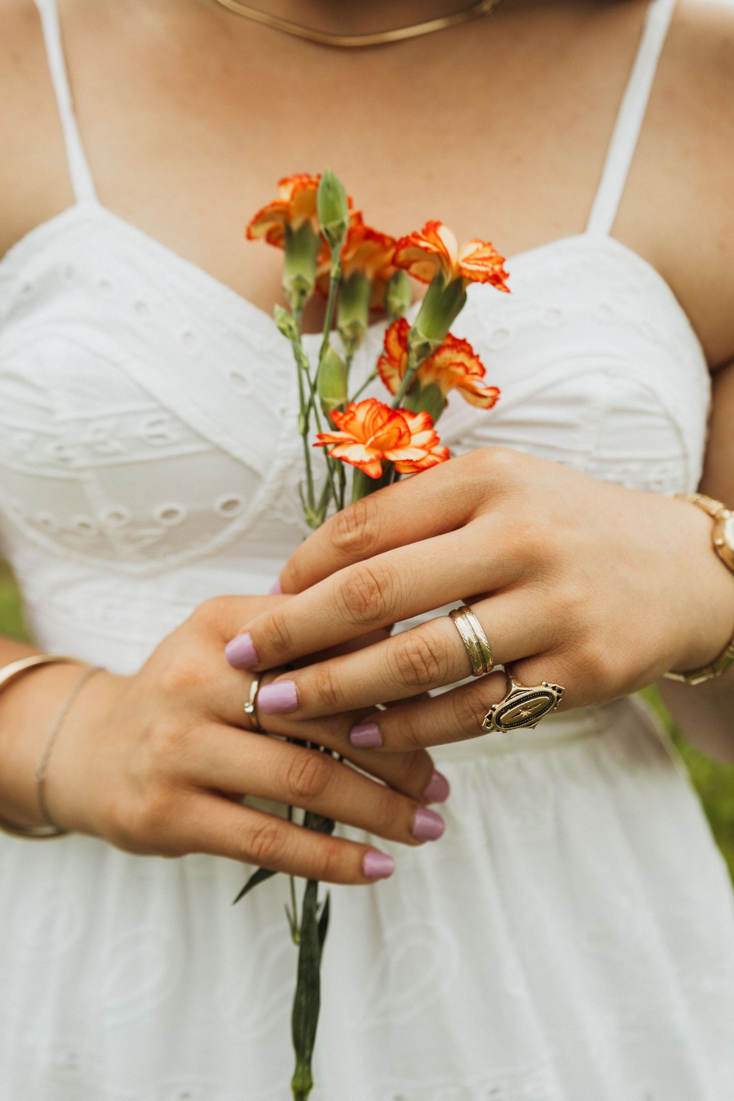 Hands wearing wedding rings hold delicate orange flowers against a white lace dress.