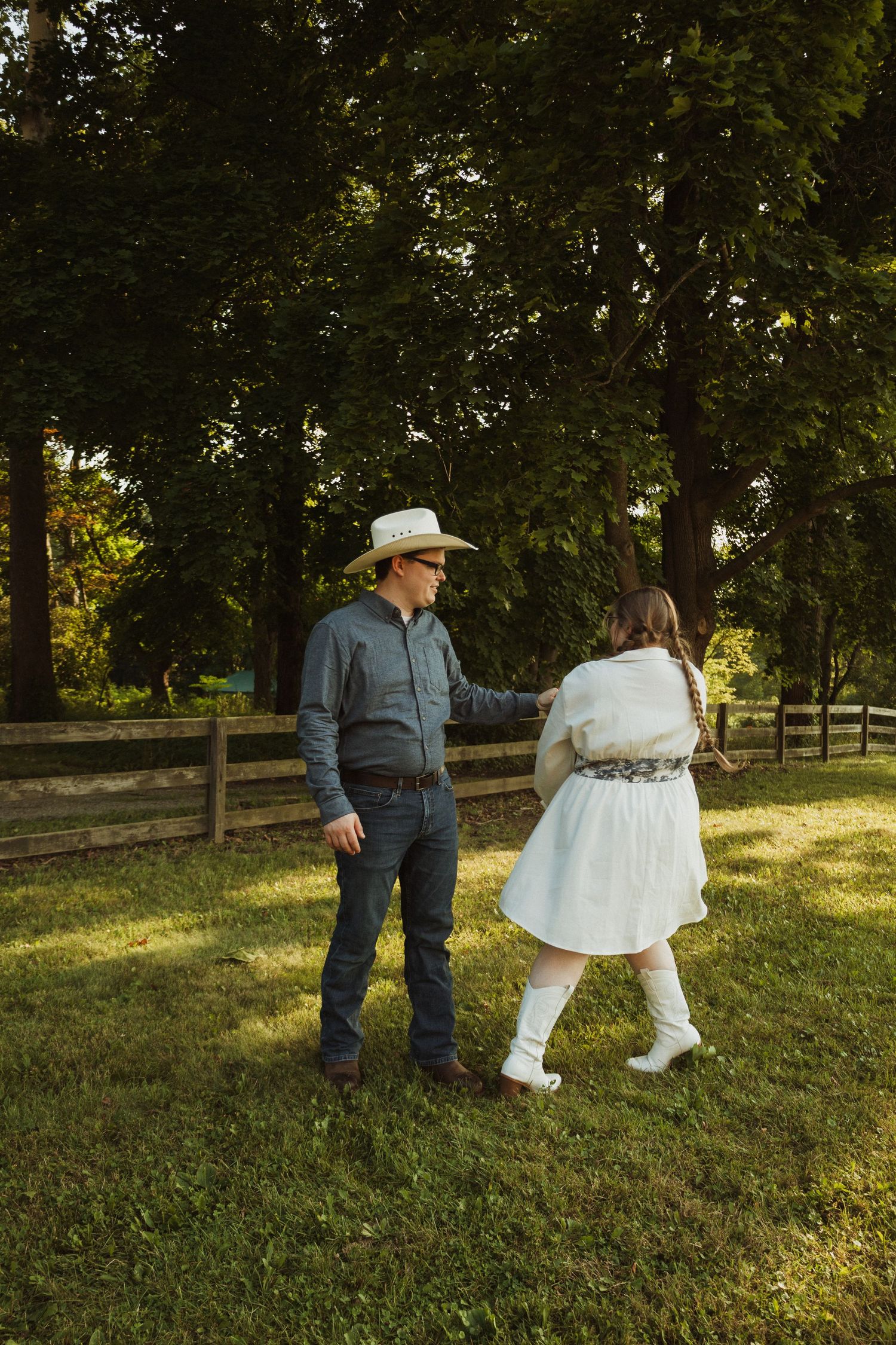 Countryside engagement photos with couple in western wear dancing on grassy slope.