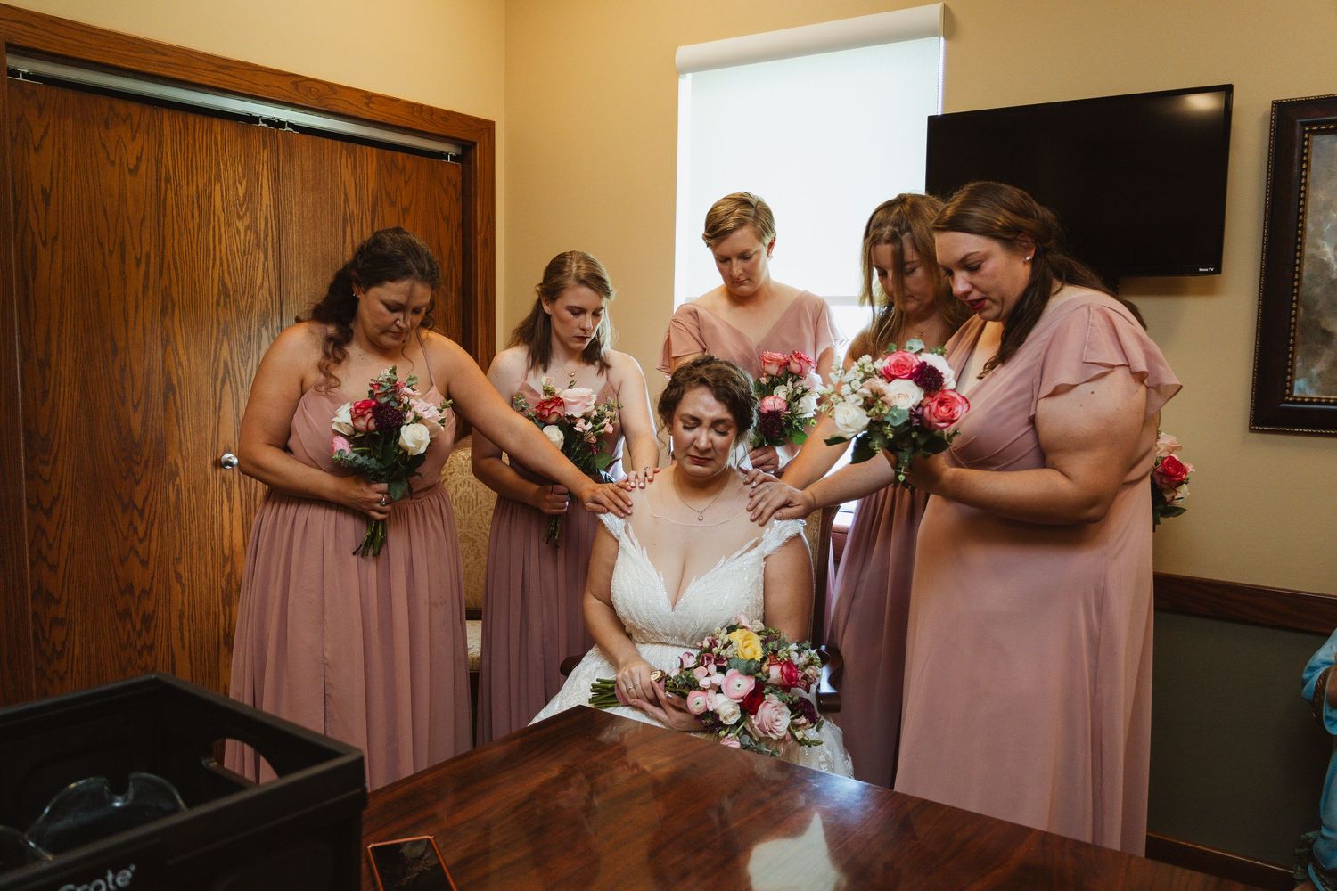 Wedding party in pink bridesmaid dresses gather for photos in an indoor venue.