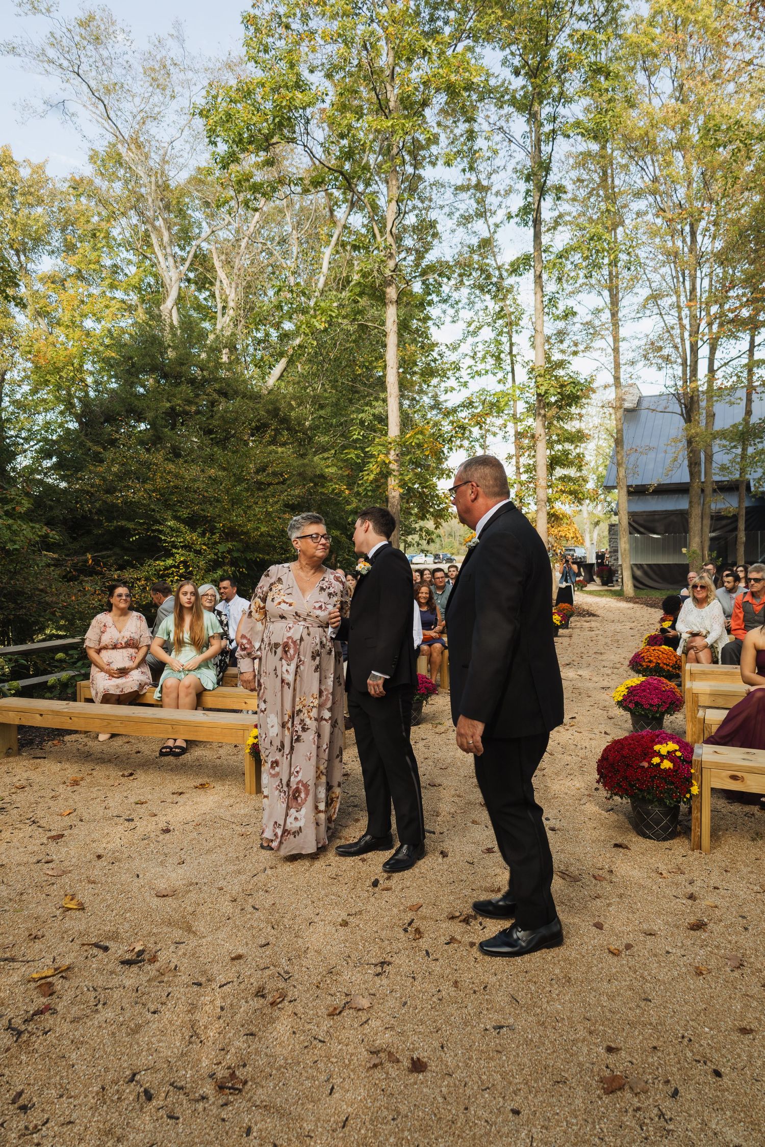 Outdoor wedding ceremony setup with wooden benches and autumn decorations in a wooded setting.