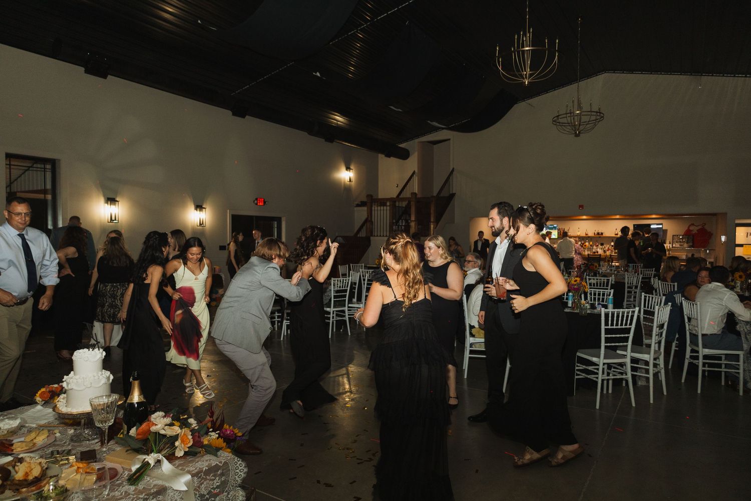 Wedding guests dancing and celebrating in a dimly lit reception hall.