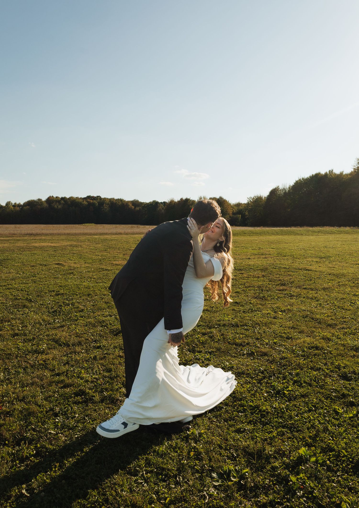 Romantic wedding couple embracing in an open field at sunset with golden light illuminating the scene.