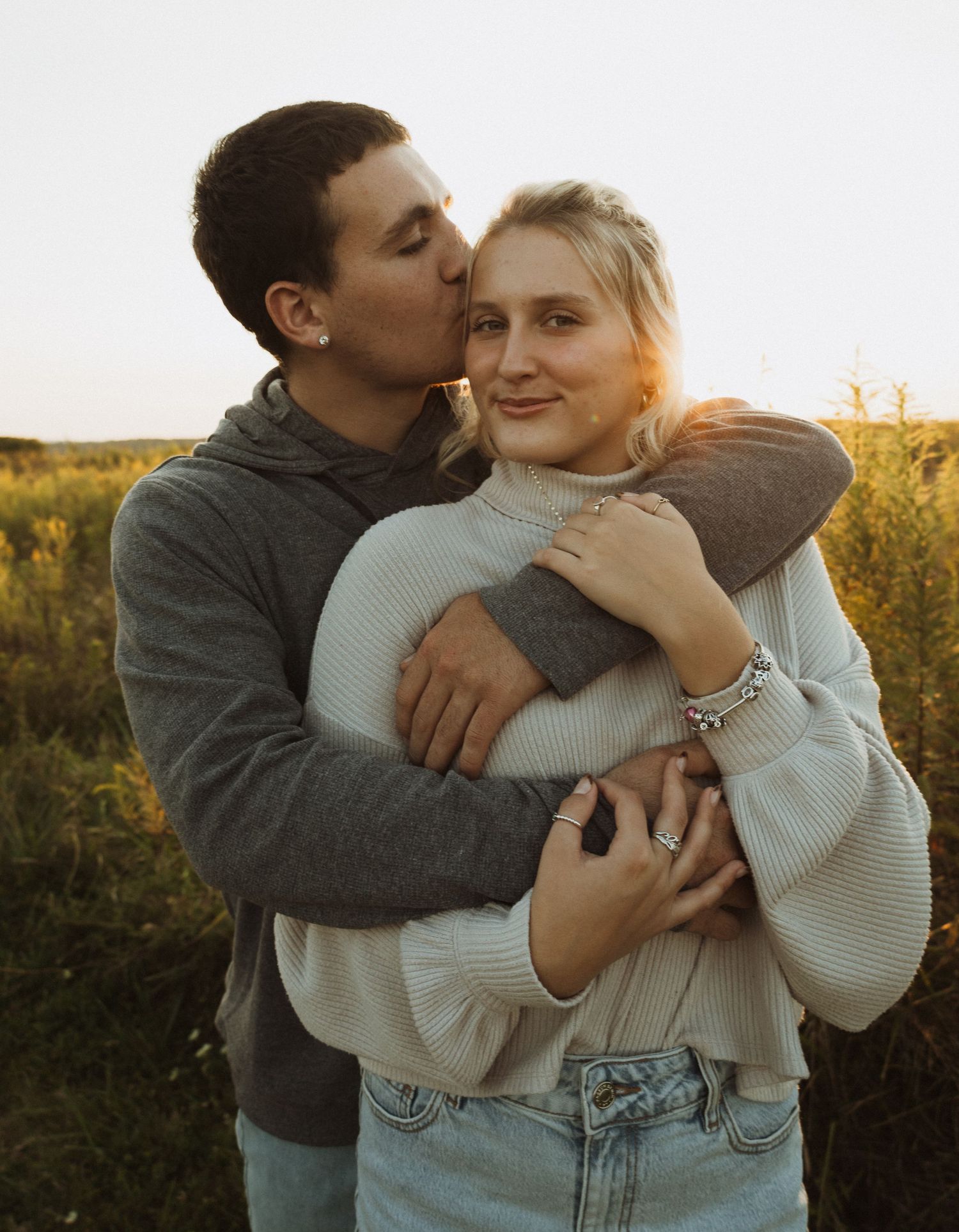 Tender embrace between couple wearing cozy sweaters in autumn field.