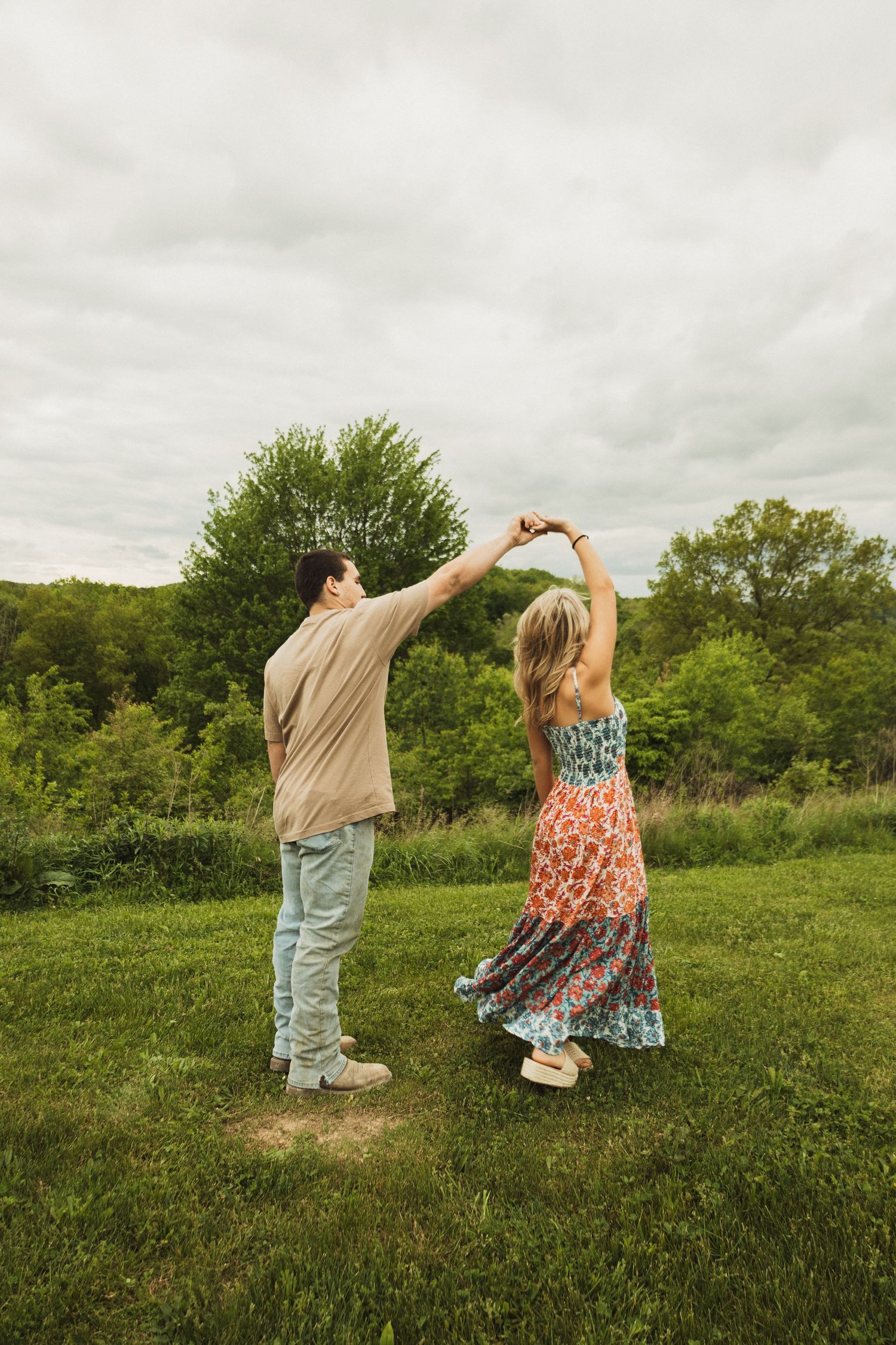 A couple dances together on a hilltop meadow with green trees in the background.