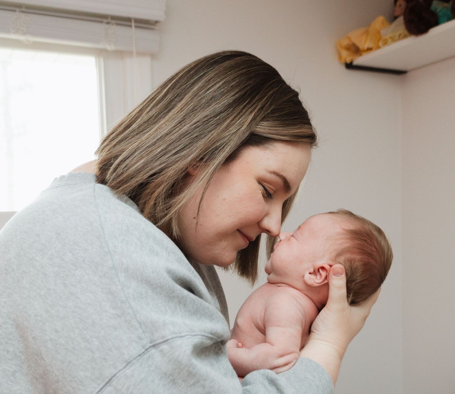 A tender moment between parent and newborn baby sharing a close embrace in a sunlit room.