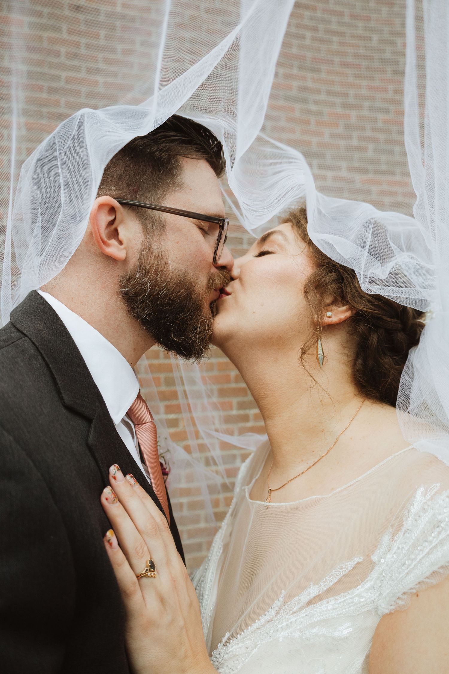 A romantic wedding portrait showing a tender kiss between newlyweds against a brick wall background.
