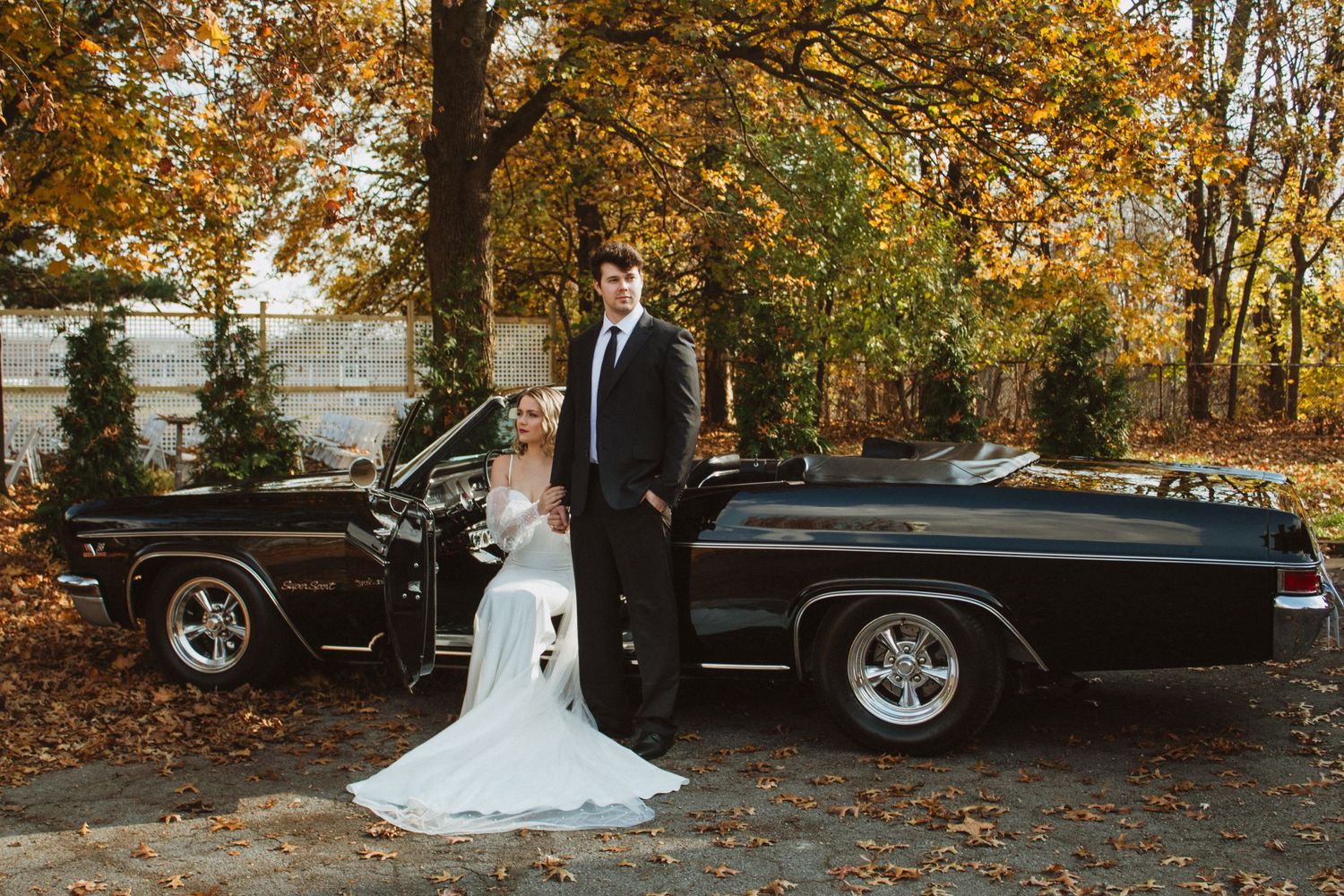A classic black vintage car serves as backdrop for a wedding photo shoot in autumn.