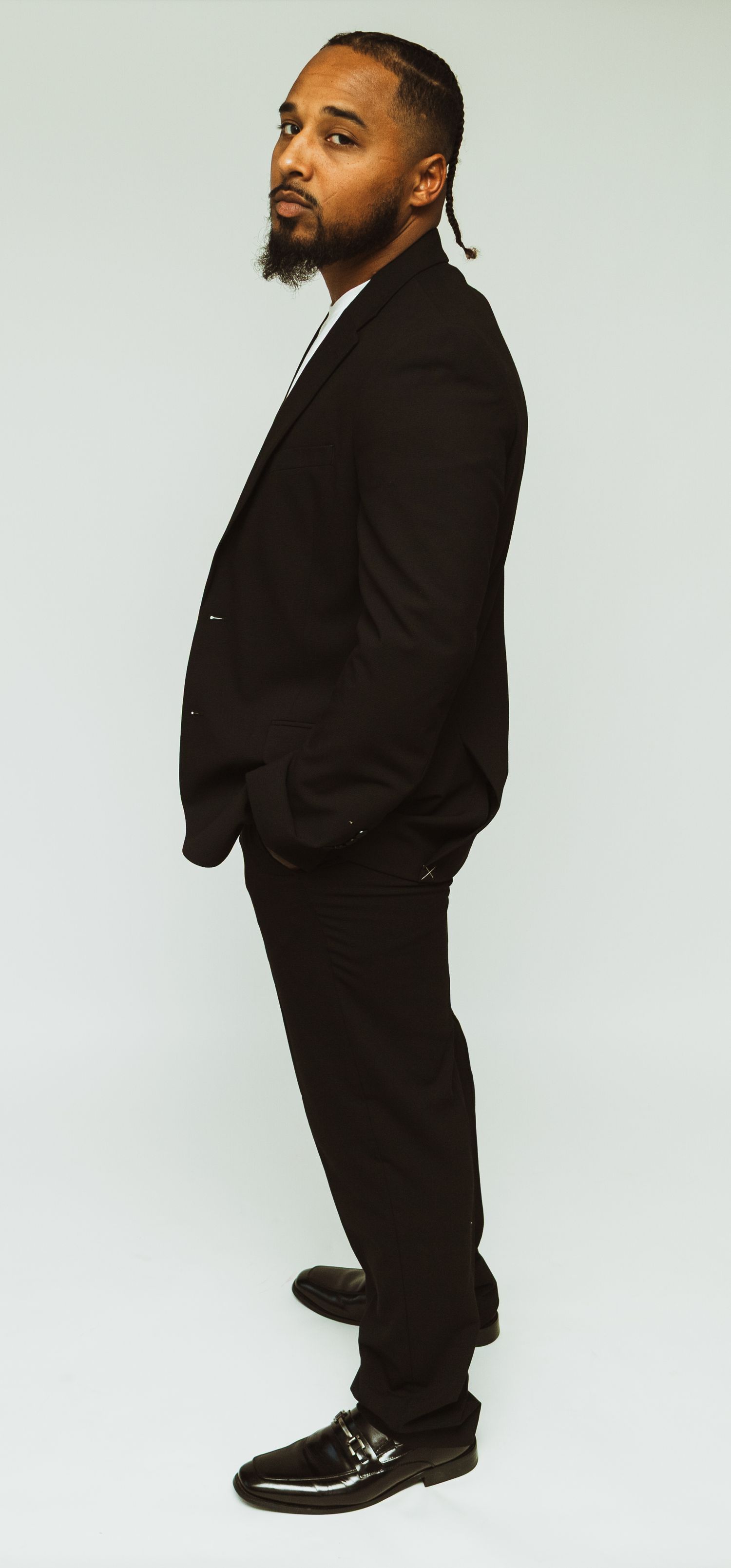 Professional studio portrait showing a person in a classic black suit standing against a white background.